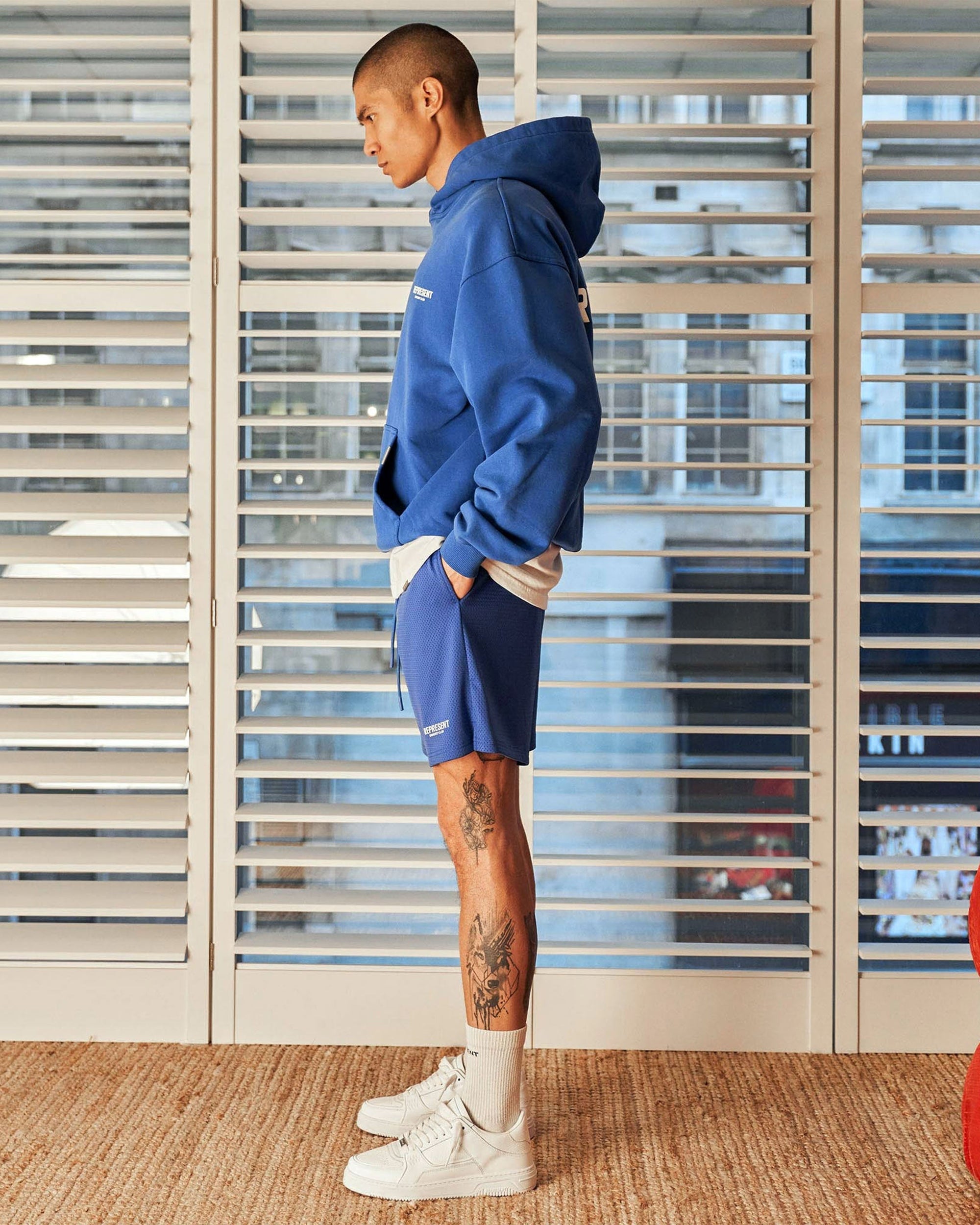 Man wearing cobalt blue mesh shorts on a plain white background | Represent Owners Club Mesh Shorts in Cobalt | Relaxed fit mesh shorts with drawcords | Owners Club Shorts | Represent Clo