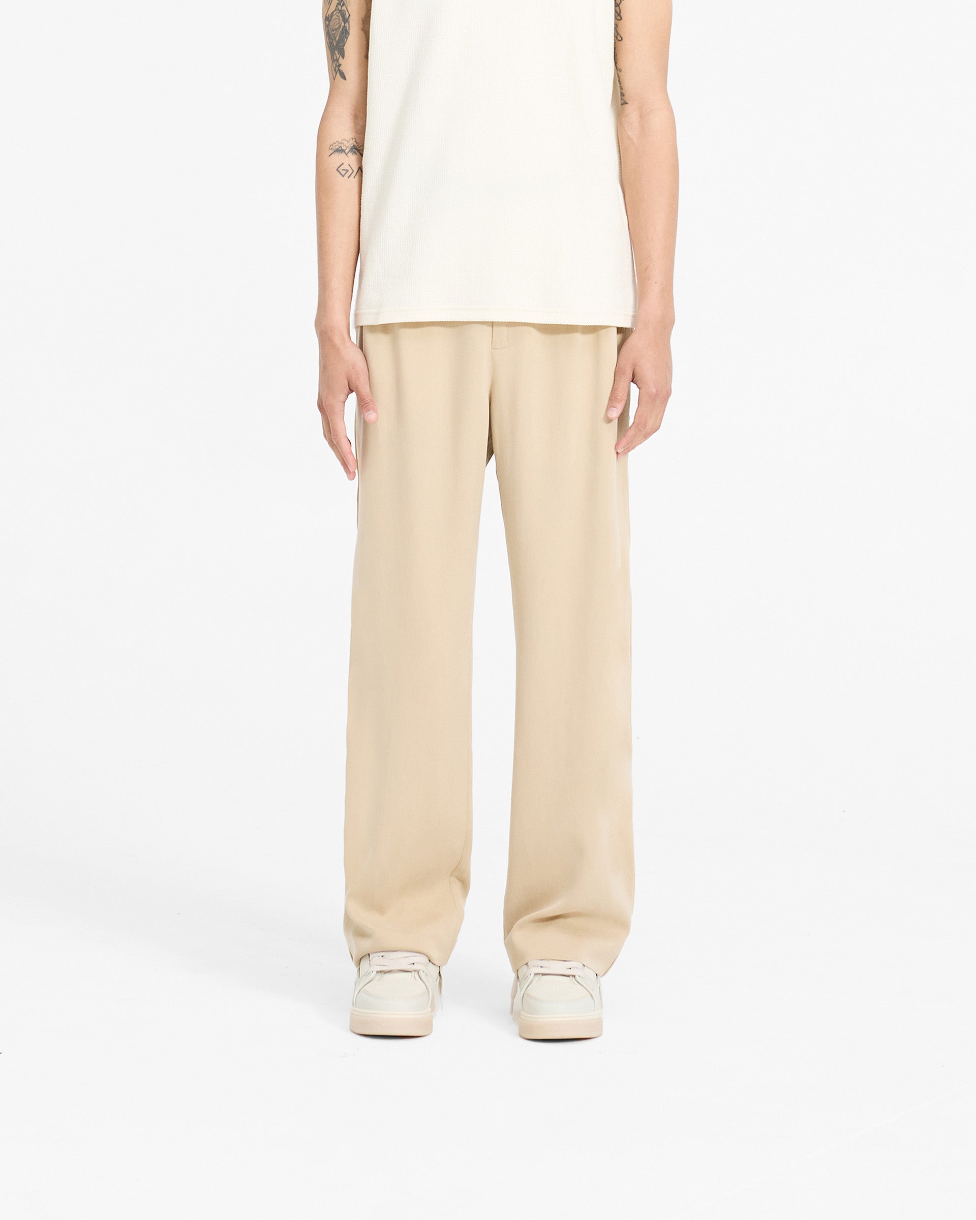 Man wearing straight leg brown pants on a plain white background | Resort Pant in Latte | Pants with hybrid waistband and ladder trim | SC24 Pants | Represent Clo