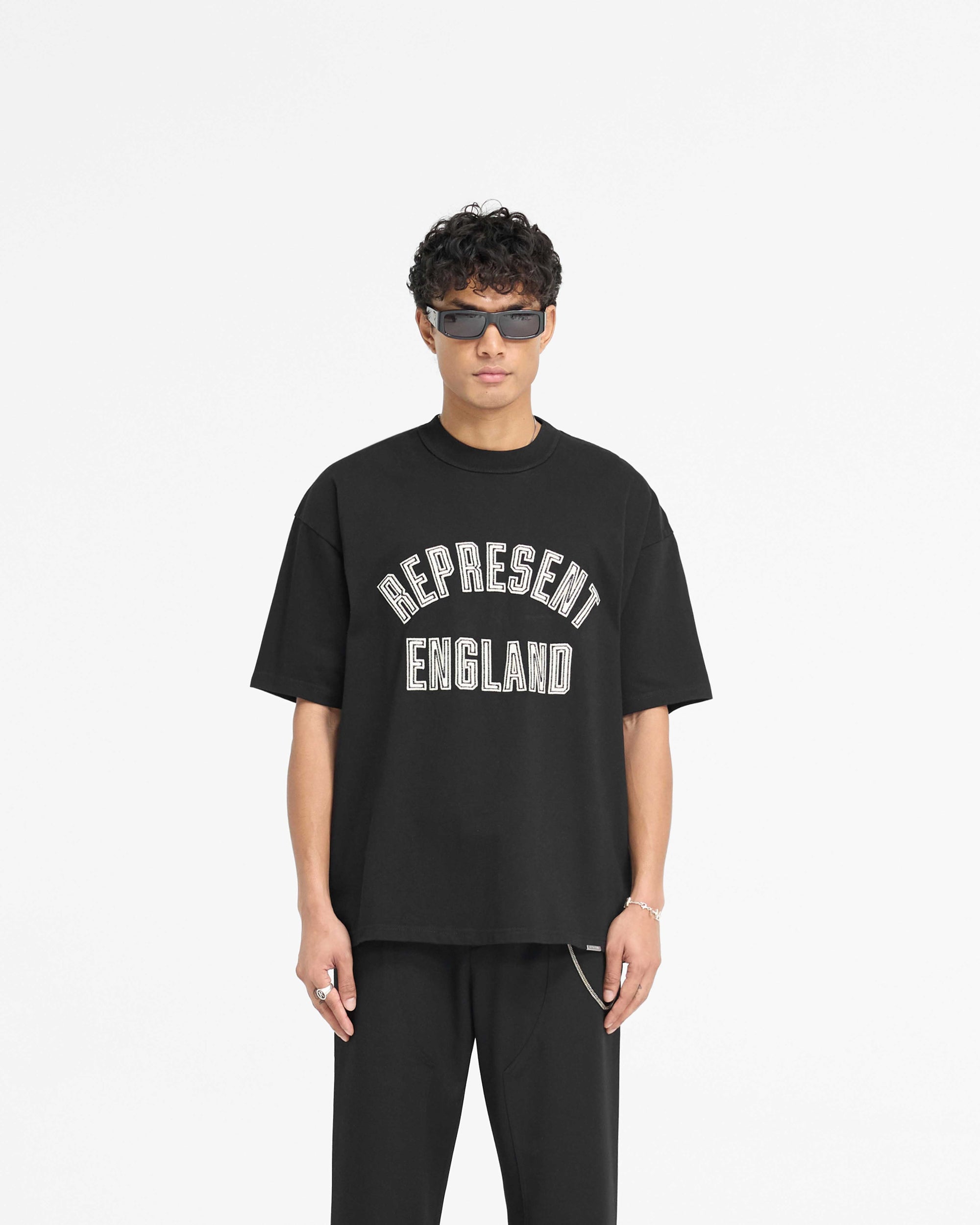 Man wearing a black t-shirt on a plain white background | England Applique T-Shirt in Jet Black | Oversized t-shirt with applique embroidery | PRE SS25 T-Shirts | Represent Clo