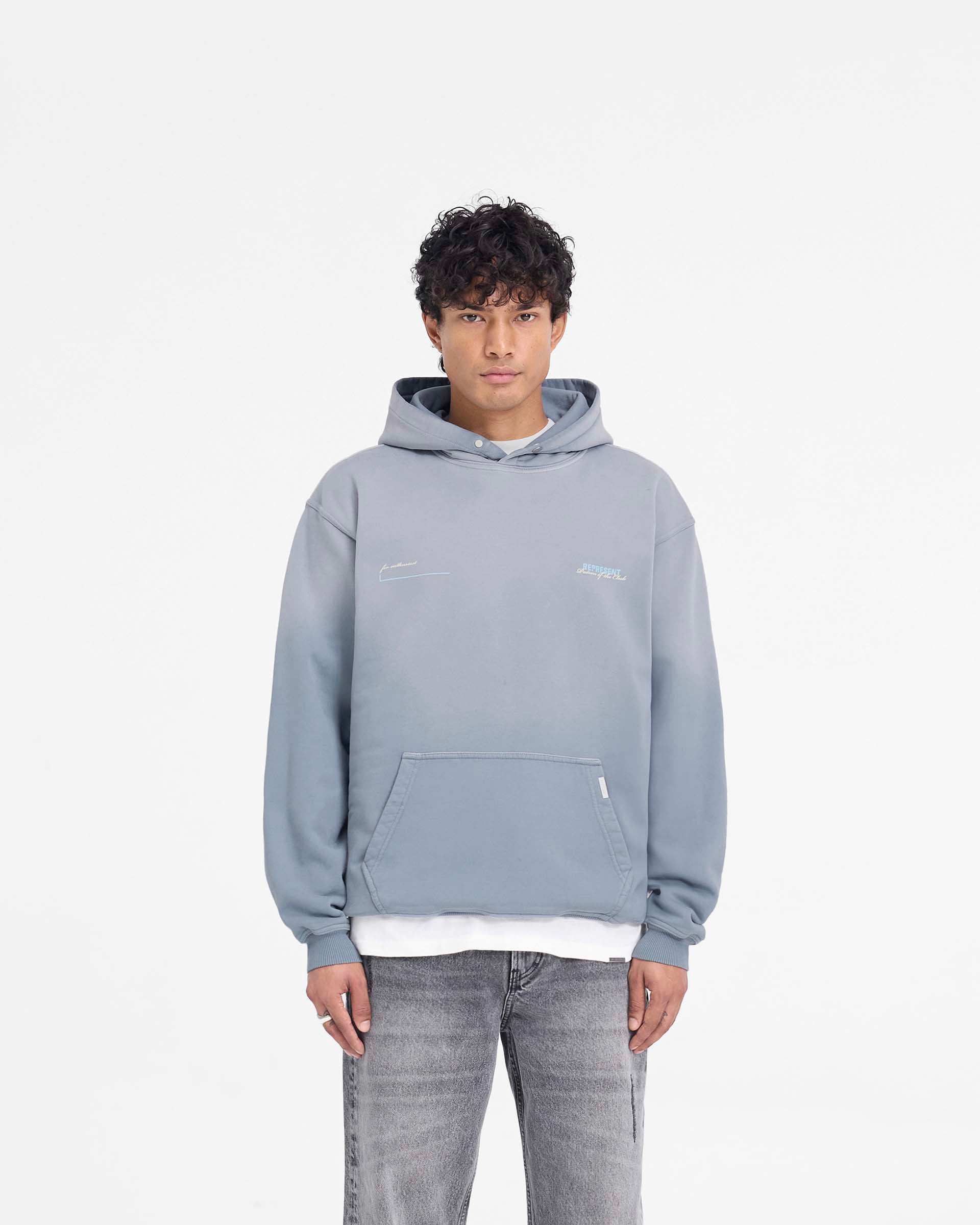 Man wearing an oversized grey hoodie on a plain white background | Patron Of The Club Hoodie in Washed Grey | Heavy weight jersey hoodie with Patron of the Club print and Cobrax popper | Patrons Hoodies | Represent Clo