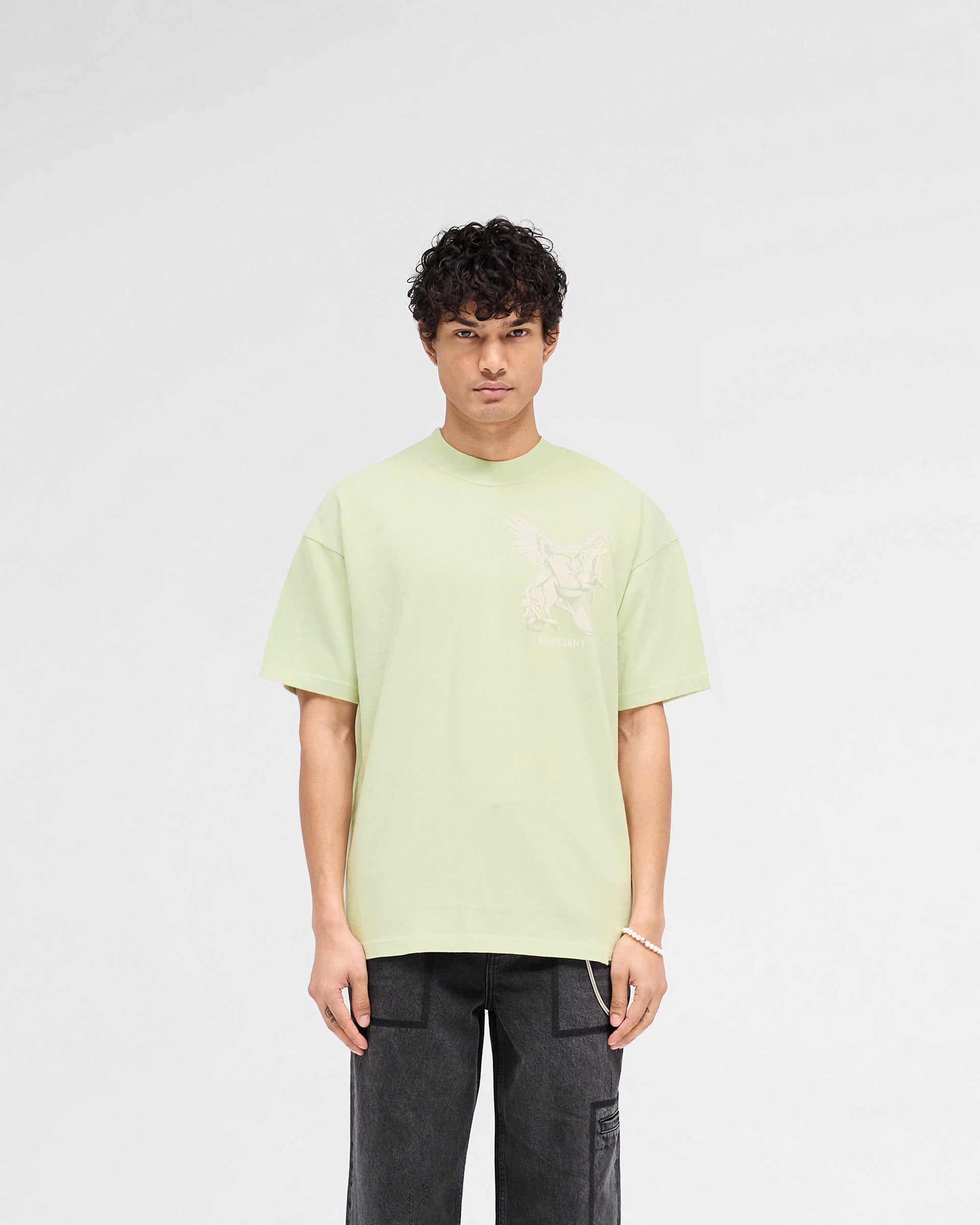 Man wearing a green oversized t-shirt on a plain white background | Elegance In Motion T-Shirt in Matcha | T-shirt with Elegance in Motion graphic and metal bar logo | SS25 T-Shirts | Represent Clo