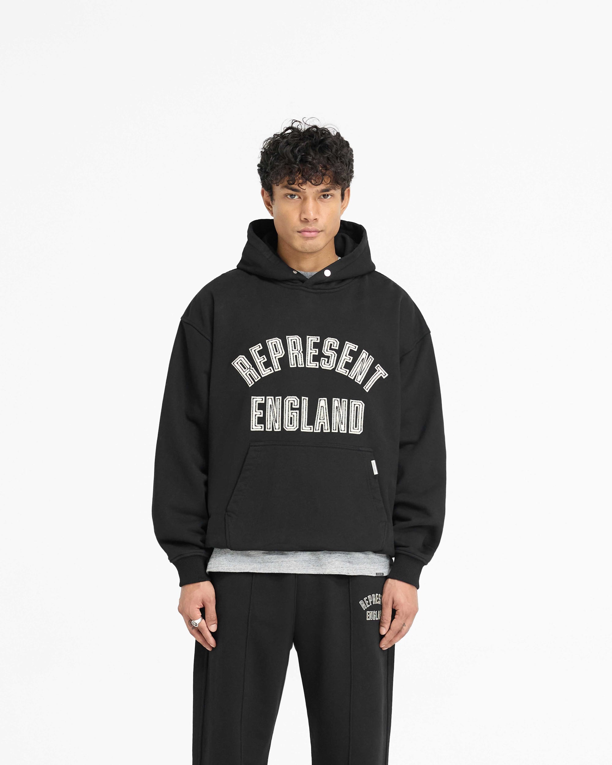 Man wearing a black hoodie on a plain white background | England Applique Hoodie in Jet Black | Slightly oversized hoodie with embroidery | PRE SS25 Hoodies | Represent Clo