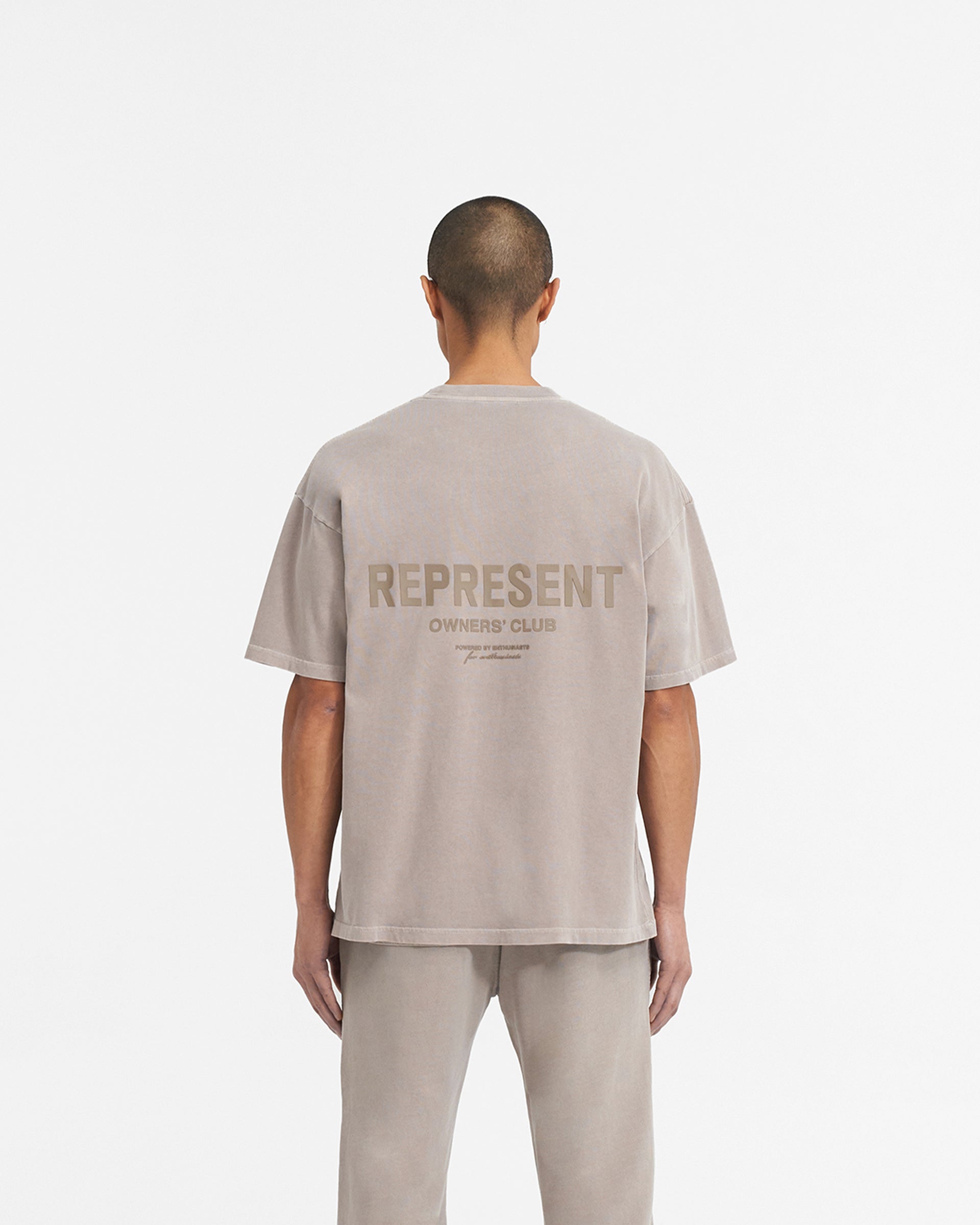 Man wearing a mushroom coloured t-shirt on a plain white background | Represent Owners Club T-Shirt in Mushroom | Short sleeve jersey tee with ribbed crewneck and high build branding | Owners Club T-Shirts | Represent Clo
