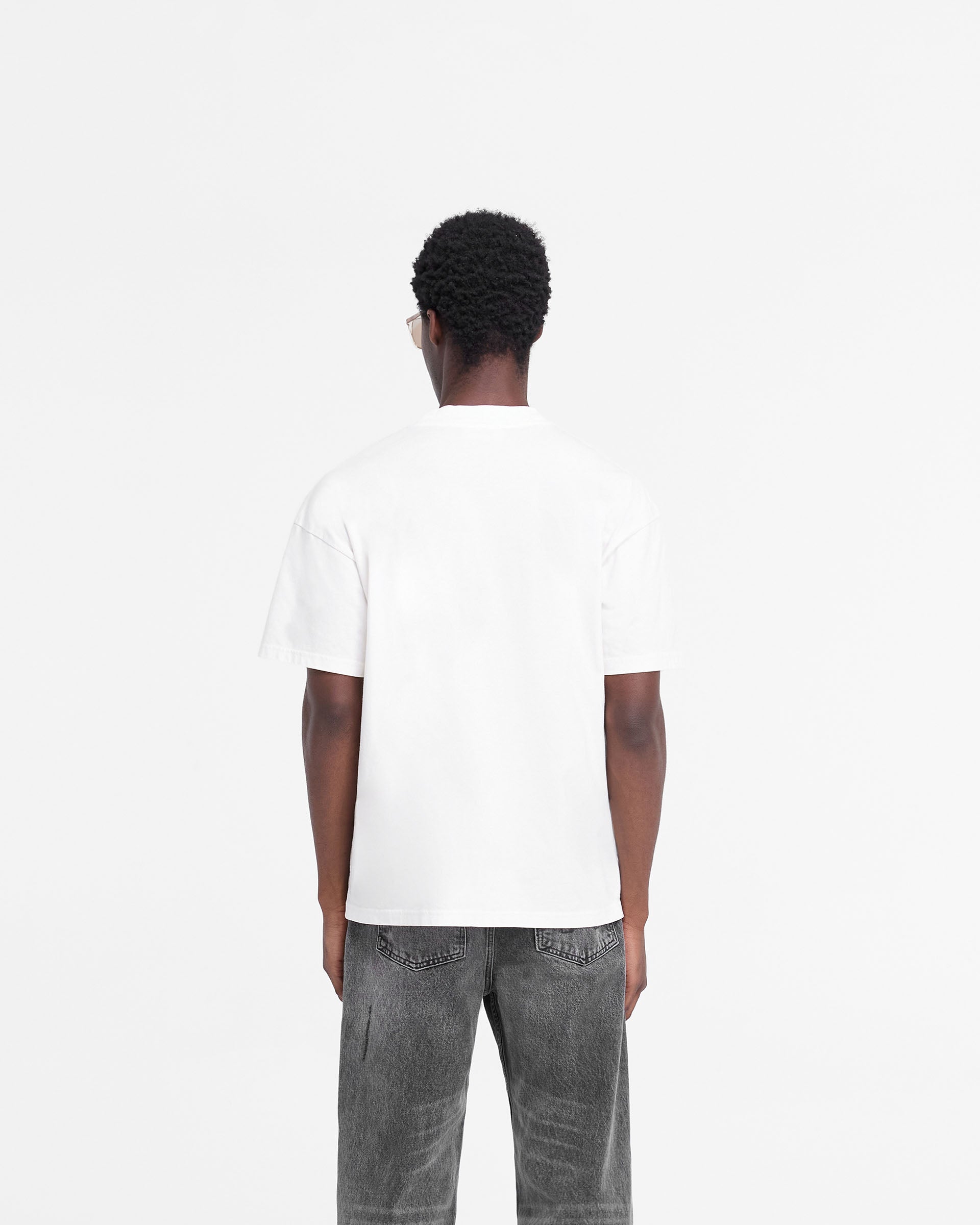 Man wearing an oversized white t-shirt on a plain white background | Rep Applique T-Shirt in Flat White | T-shirt with distressed applique logo | FW24 T-Shirts | Represent Clo