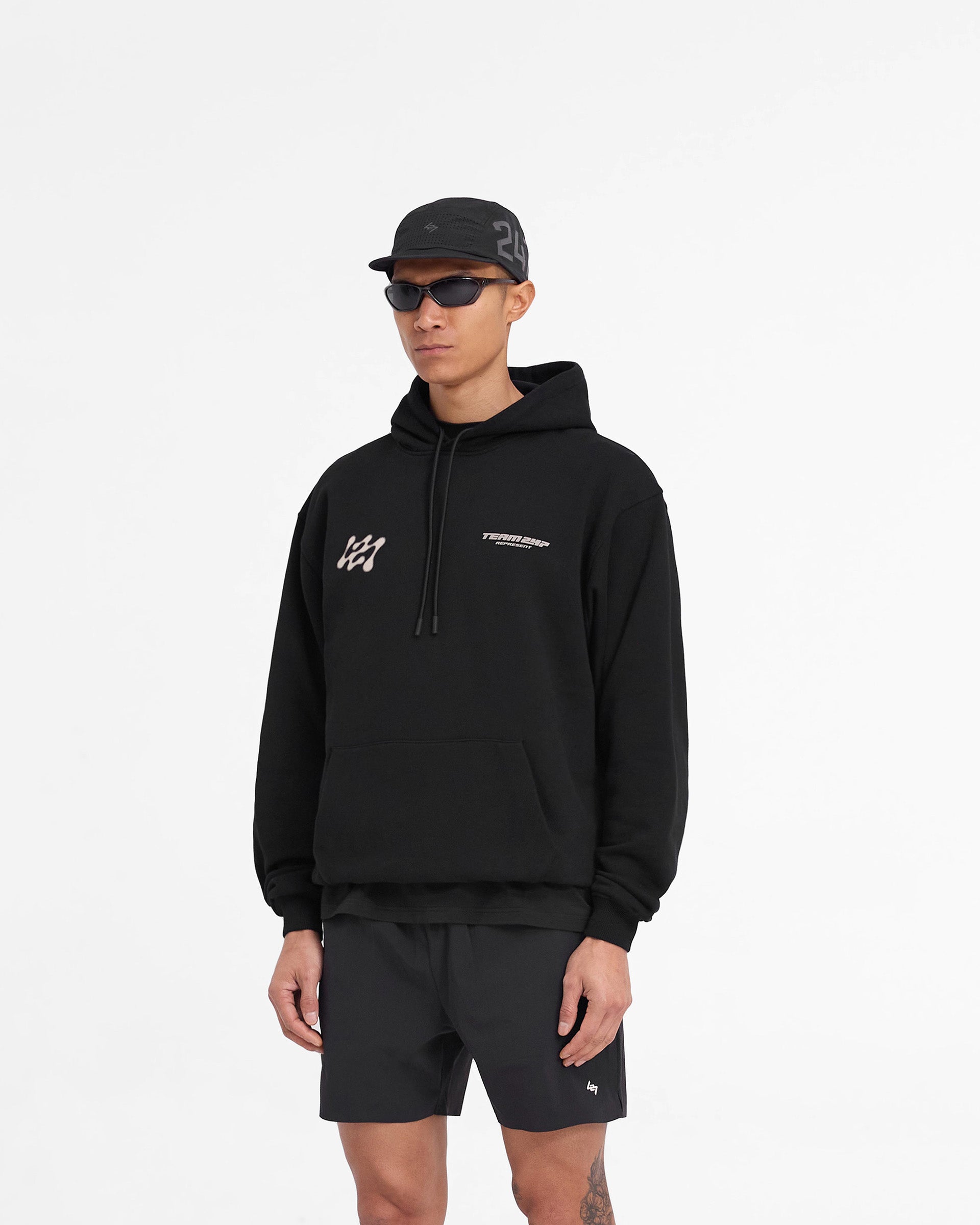 Man wearing an oversized black hoodie on a plain white background | 247 Future Terrains Oversized Hoodie in Black | Heavyweight cotton hoodie with Team 247 branding | 247 Hoodies | Represent Clo