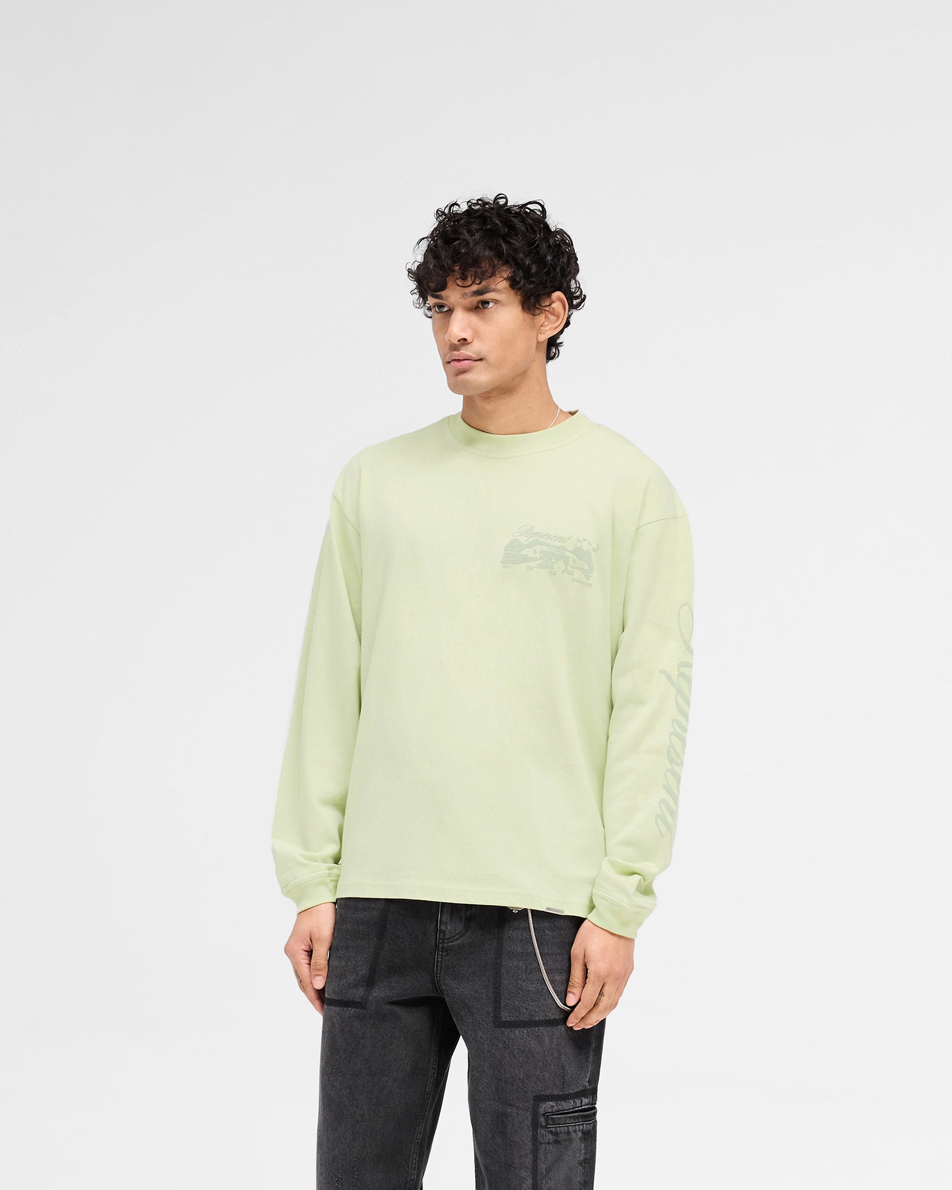 Man wearing a green long sleeve t-shirt on a plain white background | Raceway Long Sleeve T-Shirt in Matcha | Oversized t-shirt with puff print graphic and metal bar logo | SS25 T-Shirts | Represent Clo
