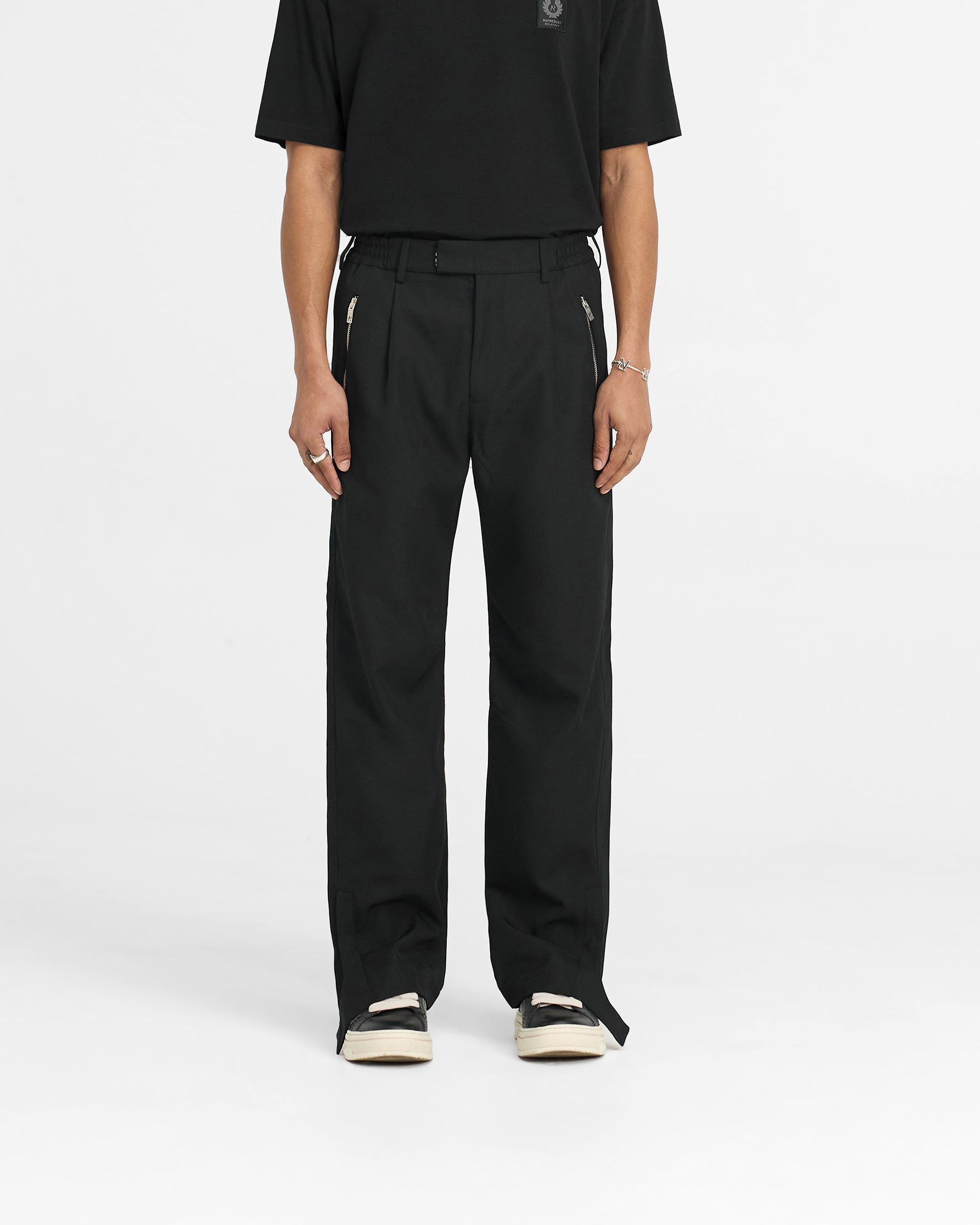 Man wearing black wool trousers on a plain white background | Represent X Belstaff Race Trouser in Black | Relaxed fit trousers with elasticated waistband and zip pockets | Exclusives Pants | Represent Clo