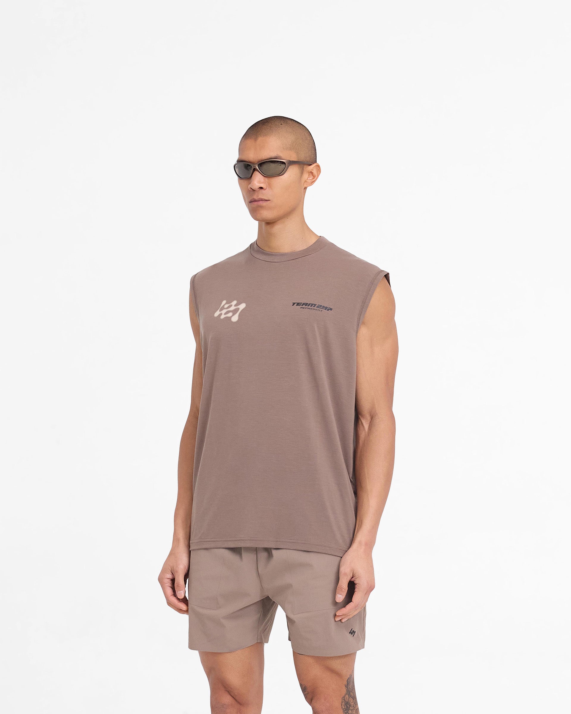 Man wearing a brown oversized tank top on a plain white background | 247 Future Terrains Oversized Tank in Umber | Oversized tank top with Future Terrains branding | 247 T-Shirts | Represent Clo