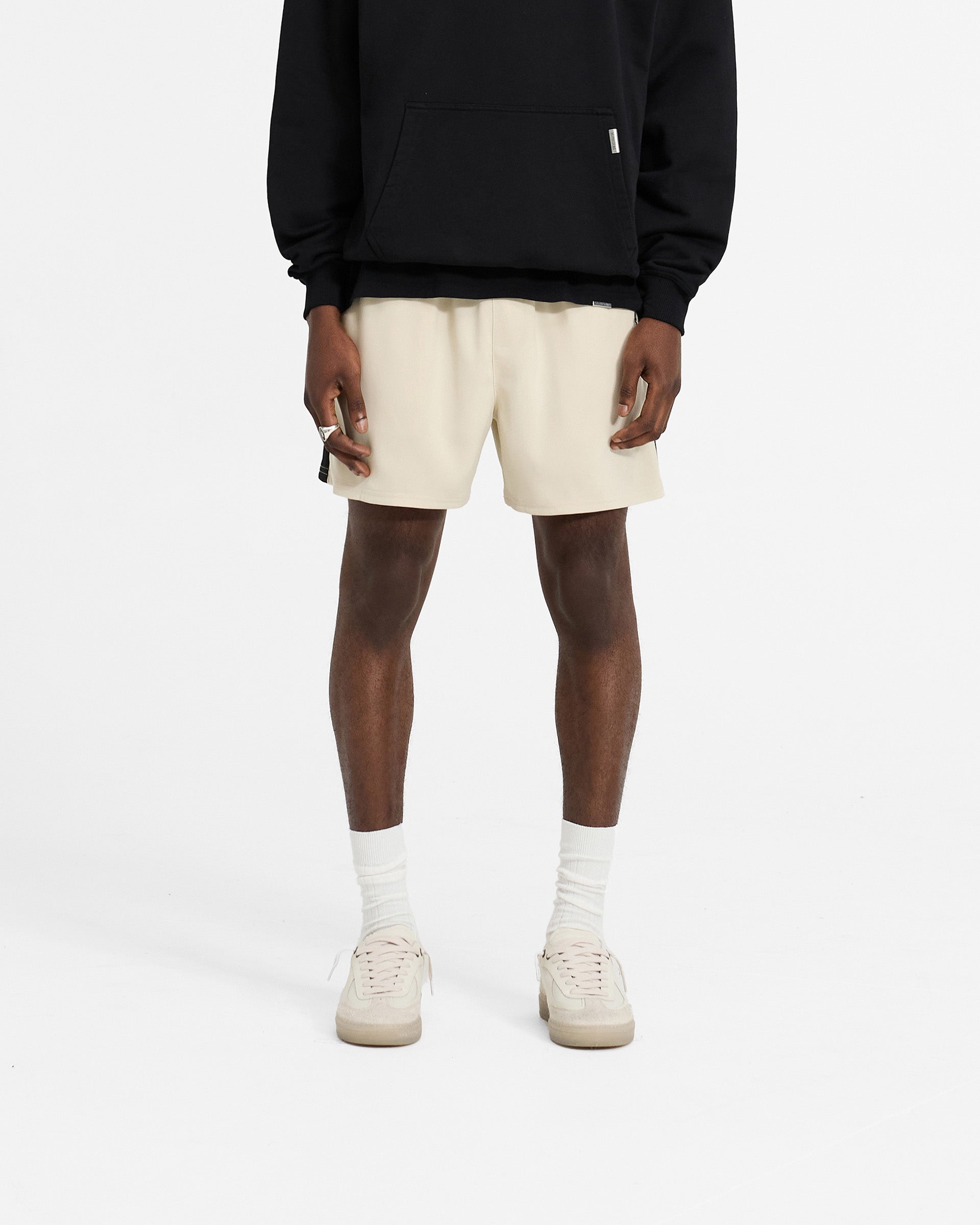 Man wearing antique white shorts on a plain white background | Track Short in Antique White | Relaxed fit track shorts with elasticated waistband | SC24 Shorts | Represent Clo