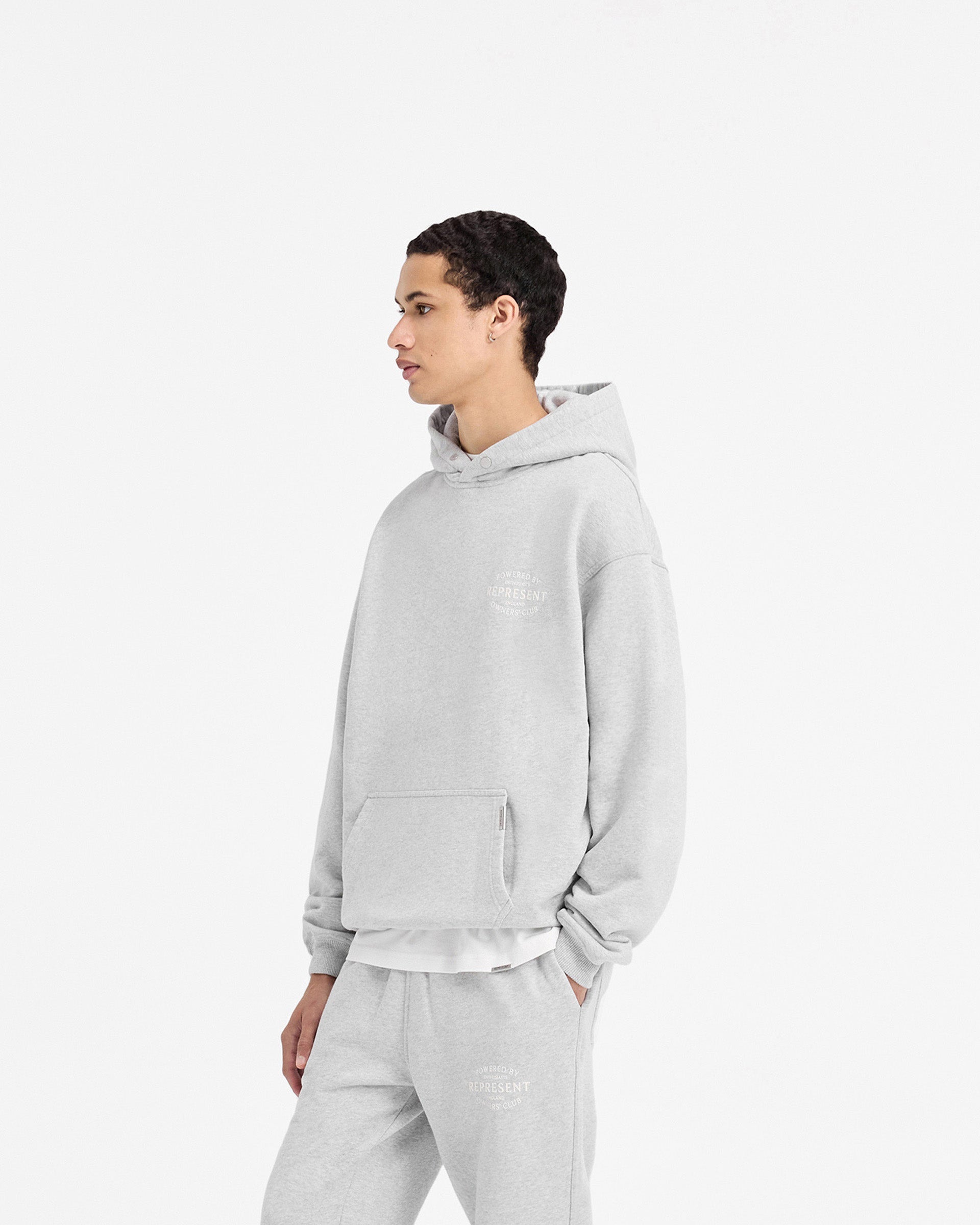 Man wearing a grey hoodie on a plain white background | Represent Owners Club Stamp Hoodie in Ash Grey | Heavy weight oversized hoodie with high build branding | Owners Club Hoodies | Represent Clo
