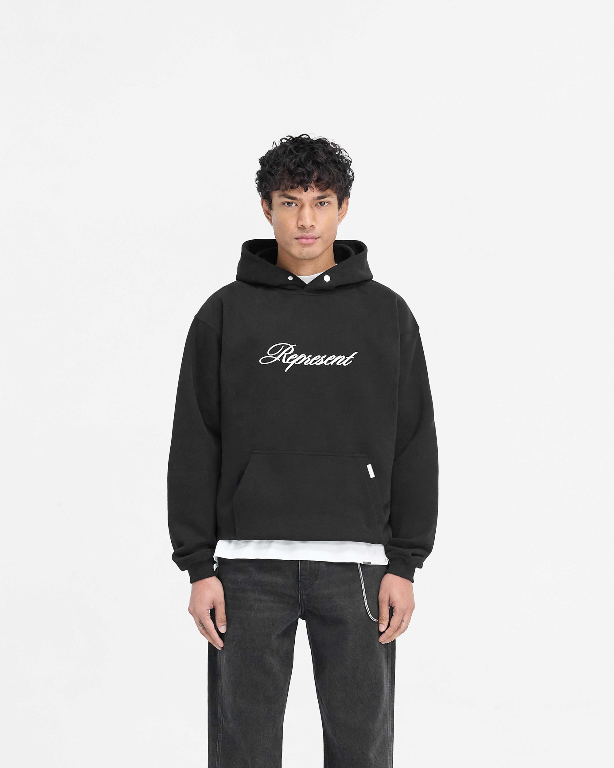 Man wearing a black hoodie on a plain white background | Script Logo Hoodie in Black | Slightly oversized hoodie with high build embroidery | PRE SS25 Hoodies | Represent Clo
