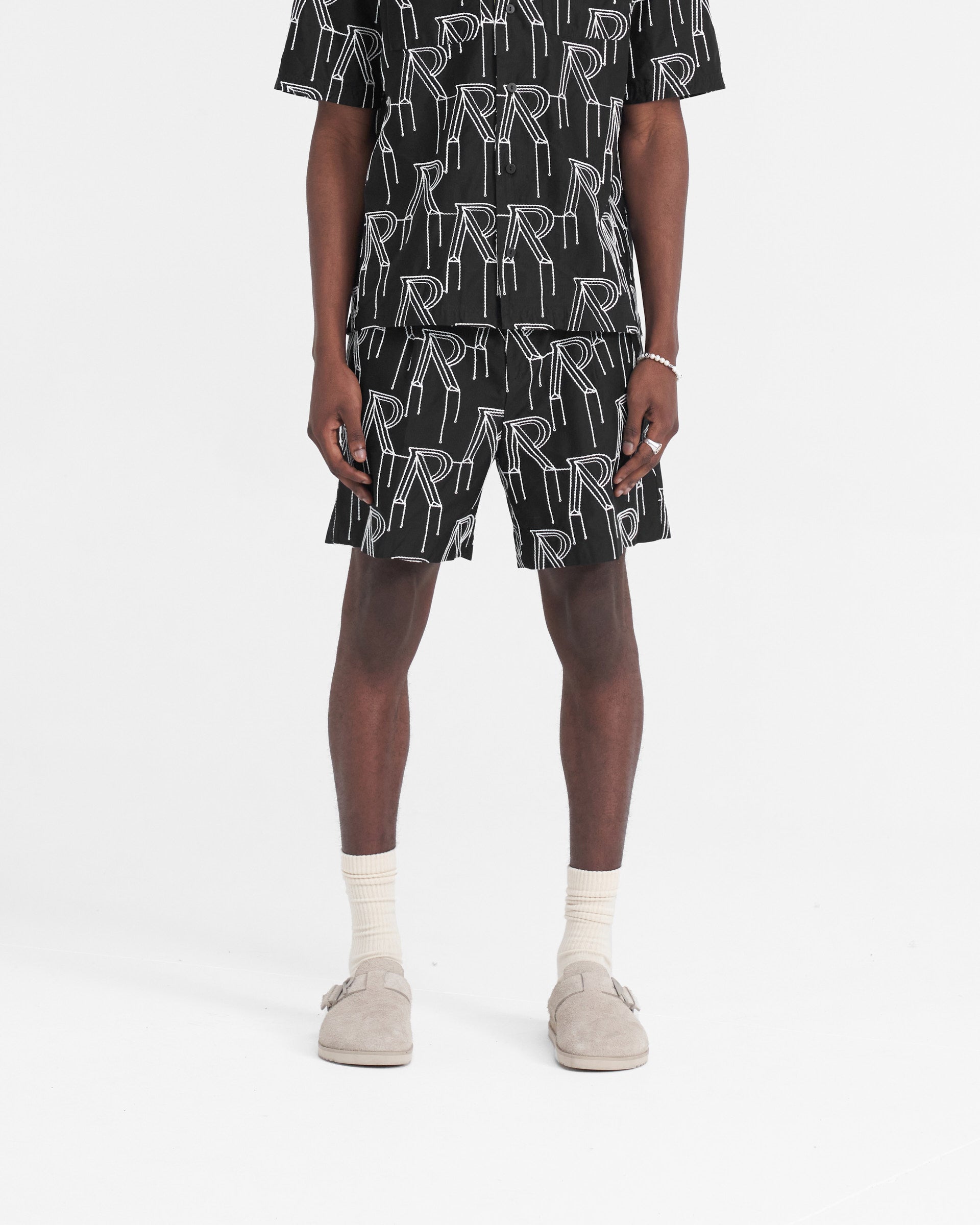 Man wearing tailored black shorts on a plain white background | Embroidered Initial Tailored Short in Black | Shorts with raised chain stitch embroidery and pleated front | SS24 Shorts | Represent Clo