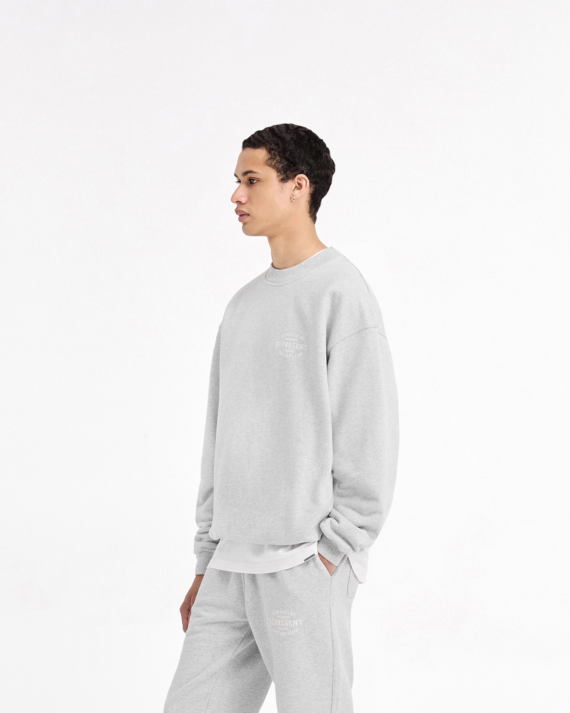 Man wearing a grey sweater on a plain white background | Represent Owners Club Stamp Sweater in Ash Grey | Sweater with ribbed hem and cuffs | Owners Club Sweaters | Represent Clo