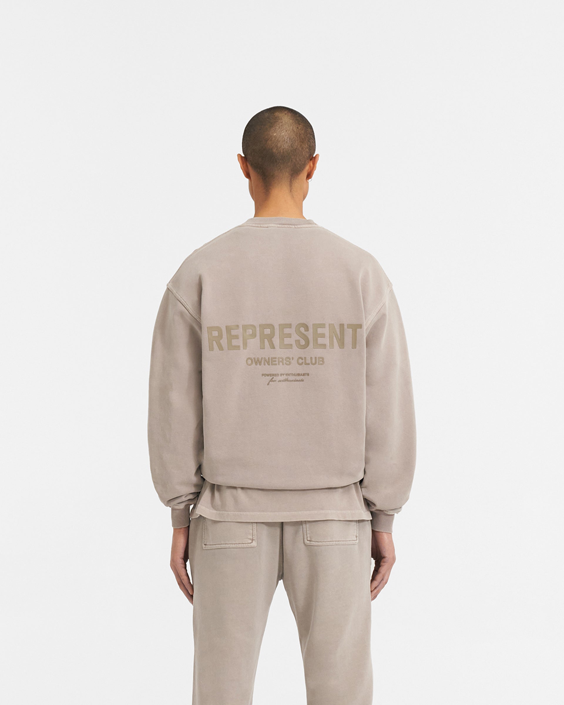 Man wearing an oversized grey sweater on a plain white background | Represent Owners Club Sweater in Mushroom | Crewneck sweater with high build branding | Owners Club Sweaters | Represent Clo