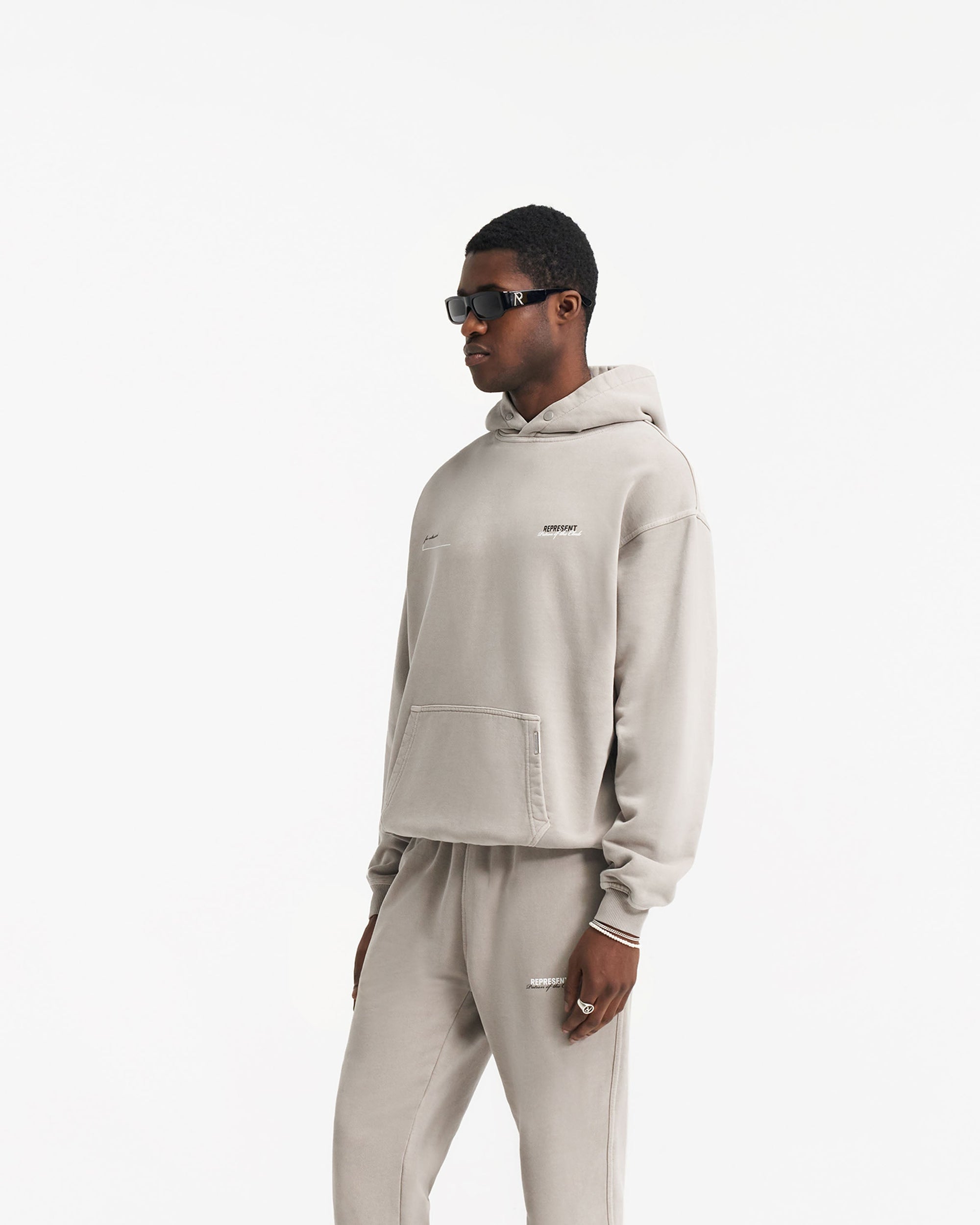 Man wearing an oversized grey hoodie on a plain white background | Patron Of The Club Hoodie in Mudstone | Heavy weight jersey cotton hoodie with ribbed trims | Patrons Hoodies | Represent Clo