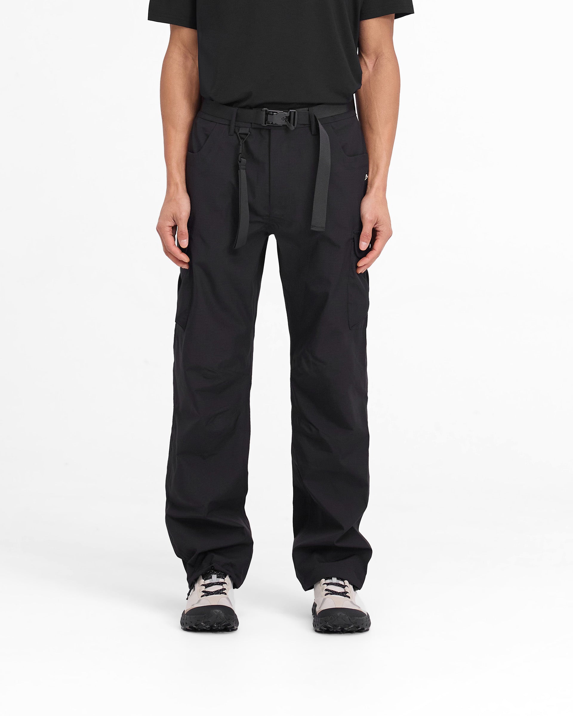 Man wearing black technical cargo pants on a plain white background | 247 Technical Cargo Pant in Black | Showerproof cargos with maglock buckle | 247 Pants | Represent Clo