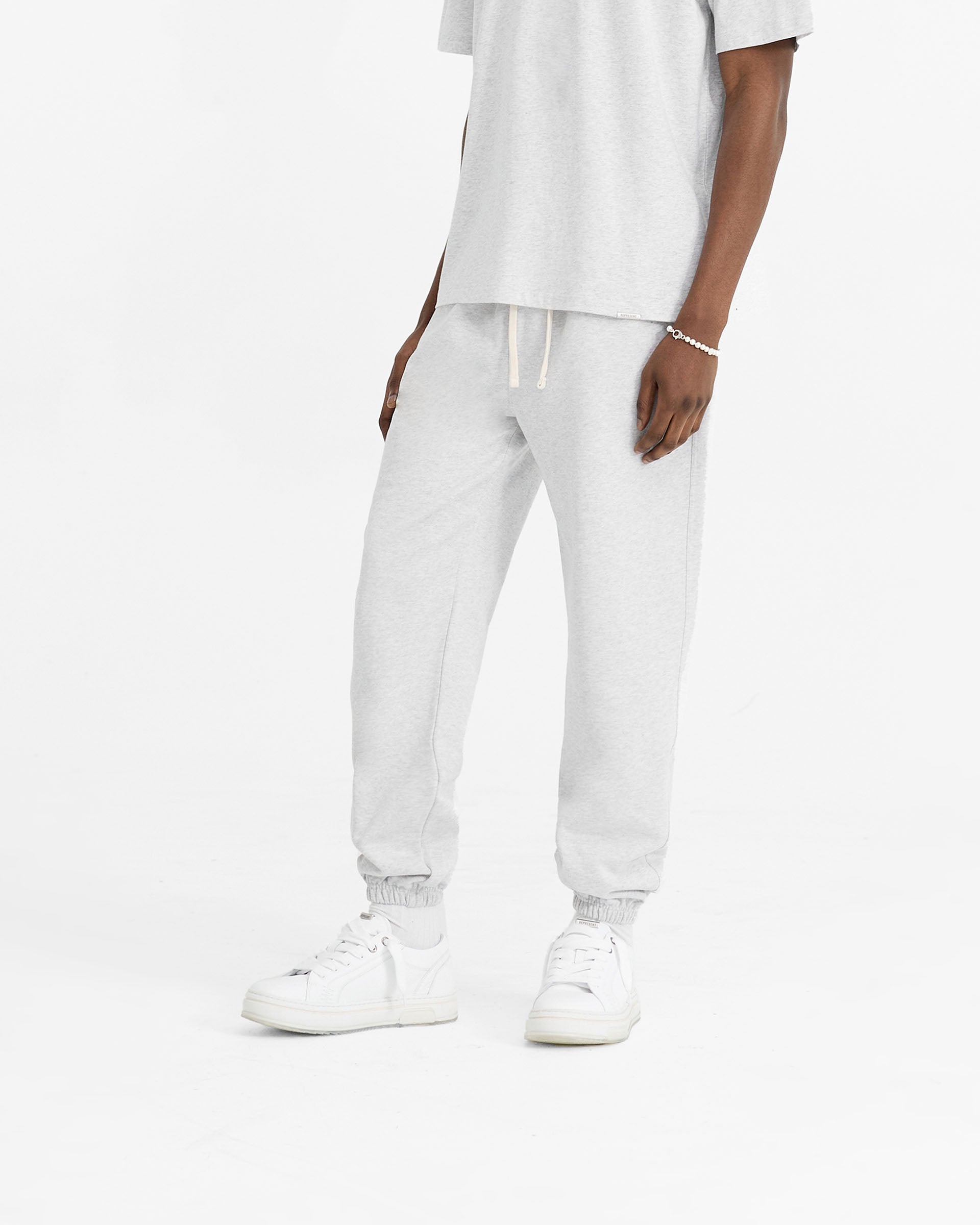 Man wearing ice grey sweatpants on a plain white background | Initial Cuffed Sweatpant in Ice Grey Marl | Heavyweight loopback cotton sweatpants with elasticated waistband | Initial Pants | Represent Clo