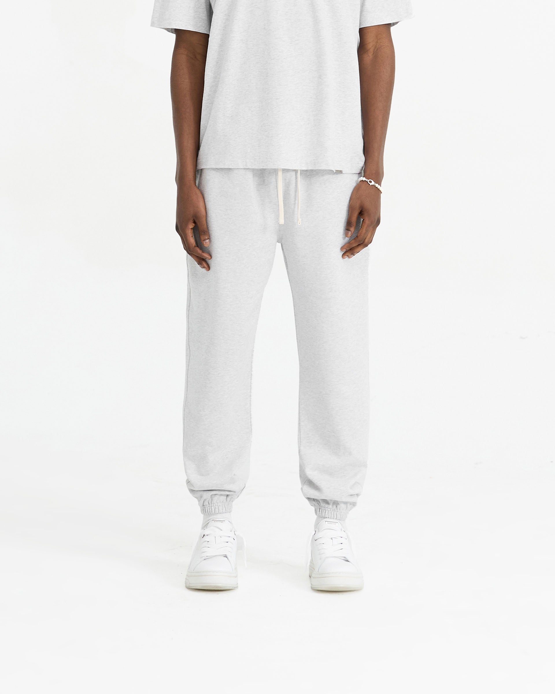 Man wearing grey sweatpants on a plain white background | Initial Cuffed Sweatpant in Ice Grey Marl | Sweatpants with elasticated waistband and cuffed hems | Initial Pants | Represent Clo