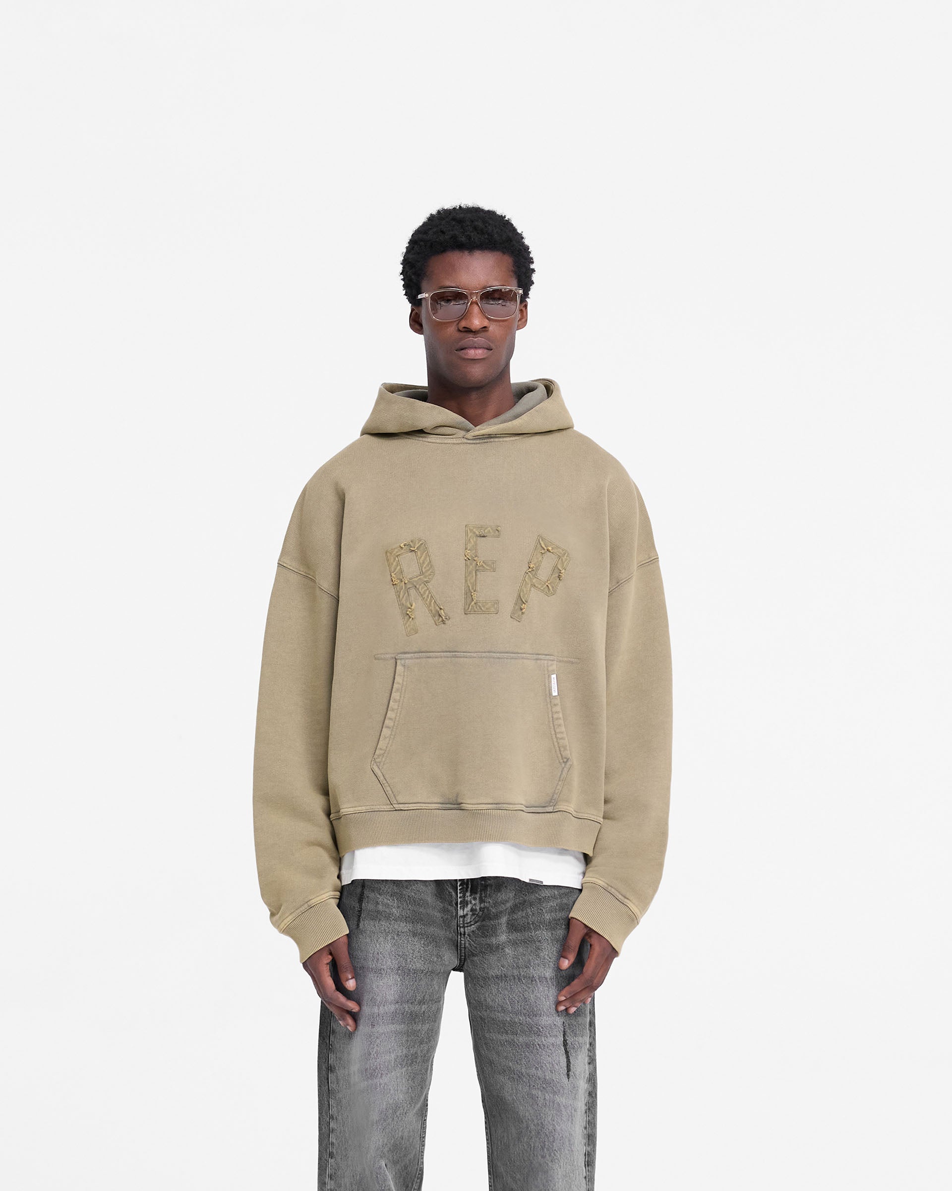 Man wearing an oversized fawn hoodie on a plain white background | Rep Applique Hoodie in Fawn | Boxy fit hoodies with sun fade wash | FW24 Hoodies | Represent Clo
