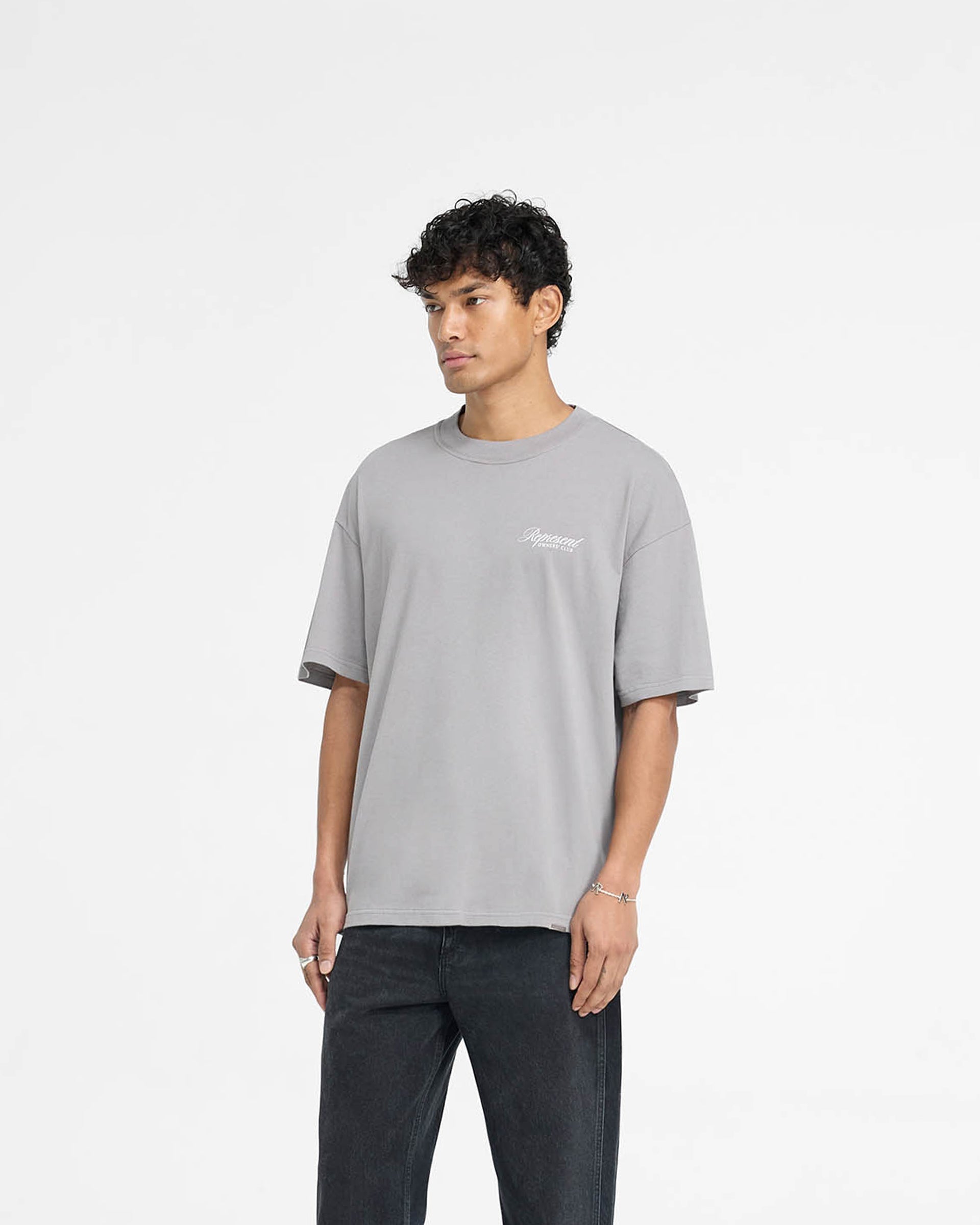 Man wearing an oversized grey t-shirt on a plain white background | Represent Owners Club Script T-Shirt in Slate | Medium weight cotton t-shirt with screen print graphic | Owners Club T-Shirts | Represent Clo
