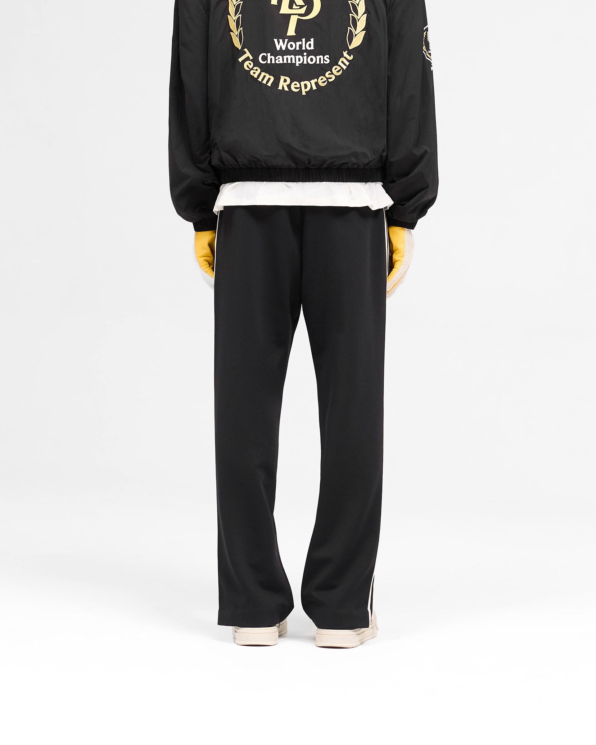 Man wearing black tailored track pants on a plain white background | Tailored Track Pant in Jet Black | Tailored pants with elasticated waistband and zip detail | SS25 Pants | Represent Clo