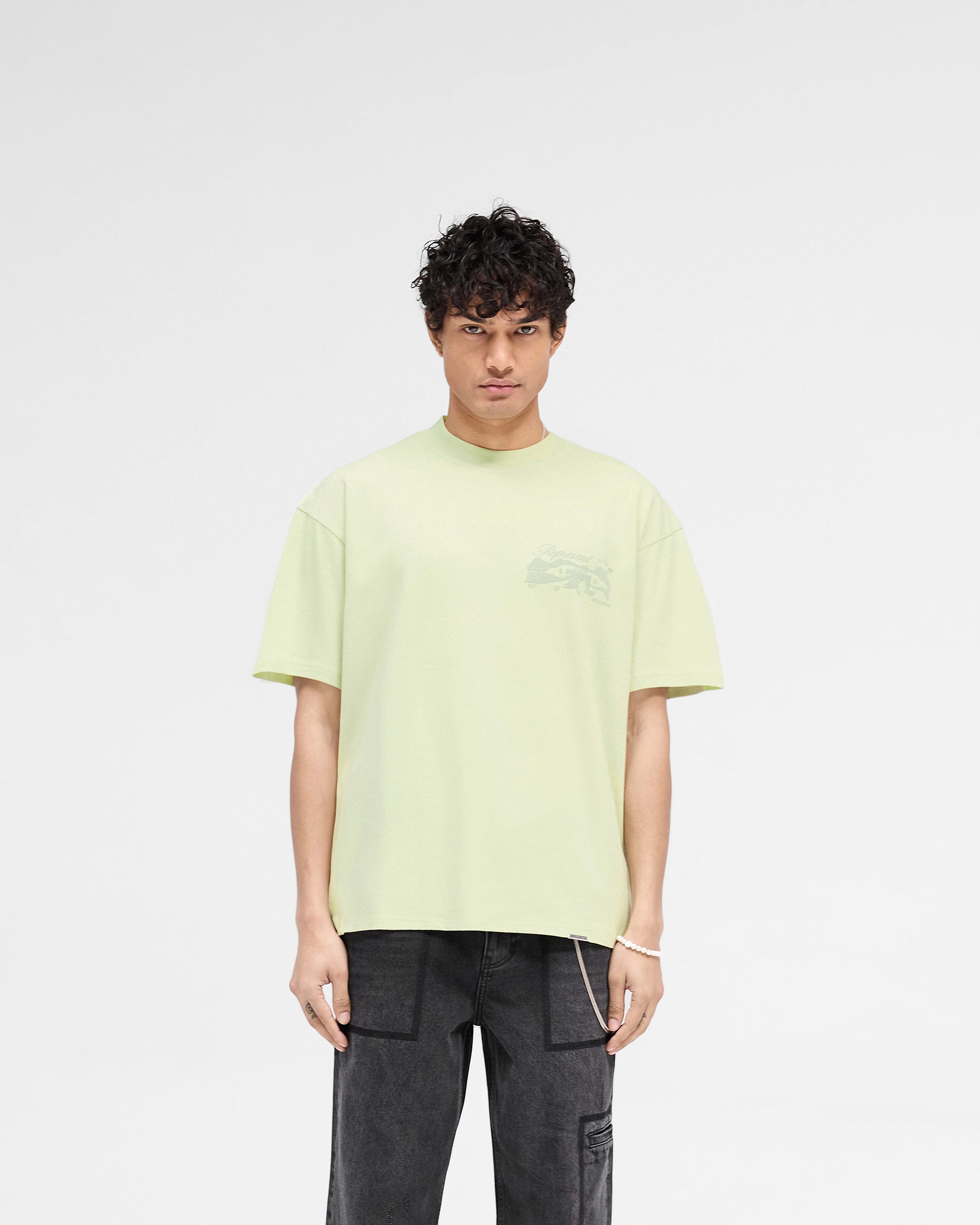Man wearing a green slightly oversized t-shirt on a plain white background | Raceway T-Shirt in Matcha | T-Shirt with puff print graphic and metal bar logo | SS25 T-Shirts | Represent Clo