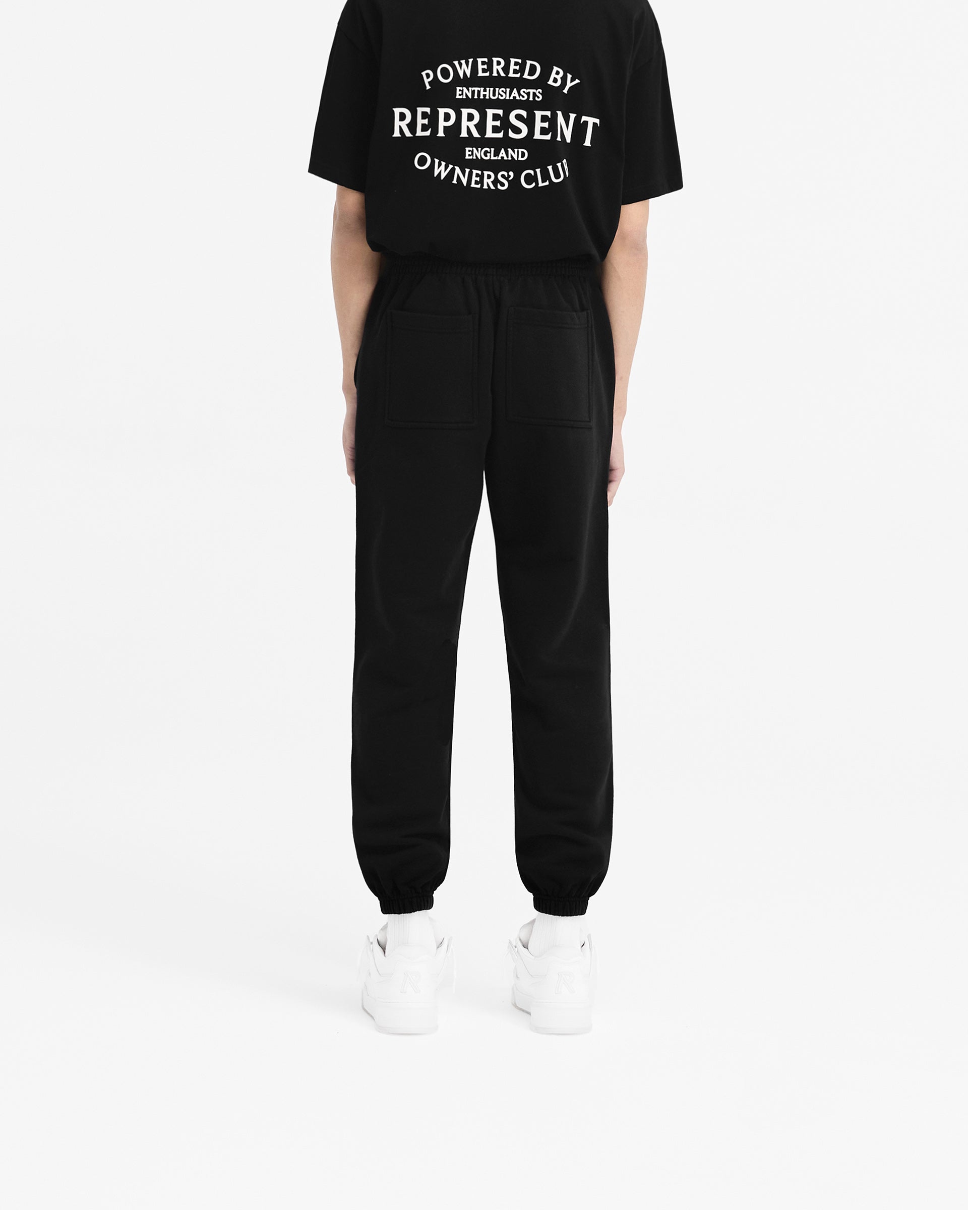 Man wearing black sweatpants on a plain white background | Represent Owners Club Stamp Sweatpant in Jet Black | Sweatpants with elasticated waistband and welt pockets | Owners Club Pants | Represent Clo
