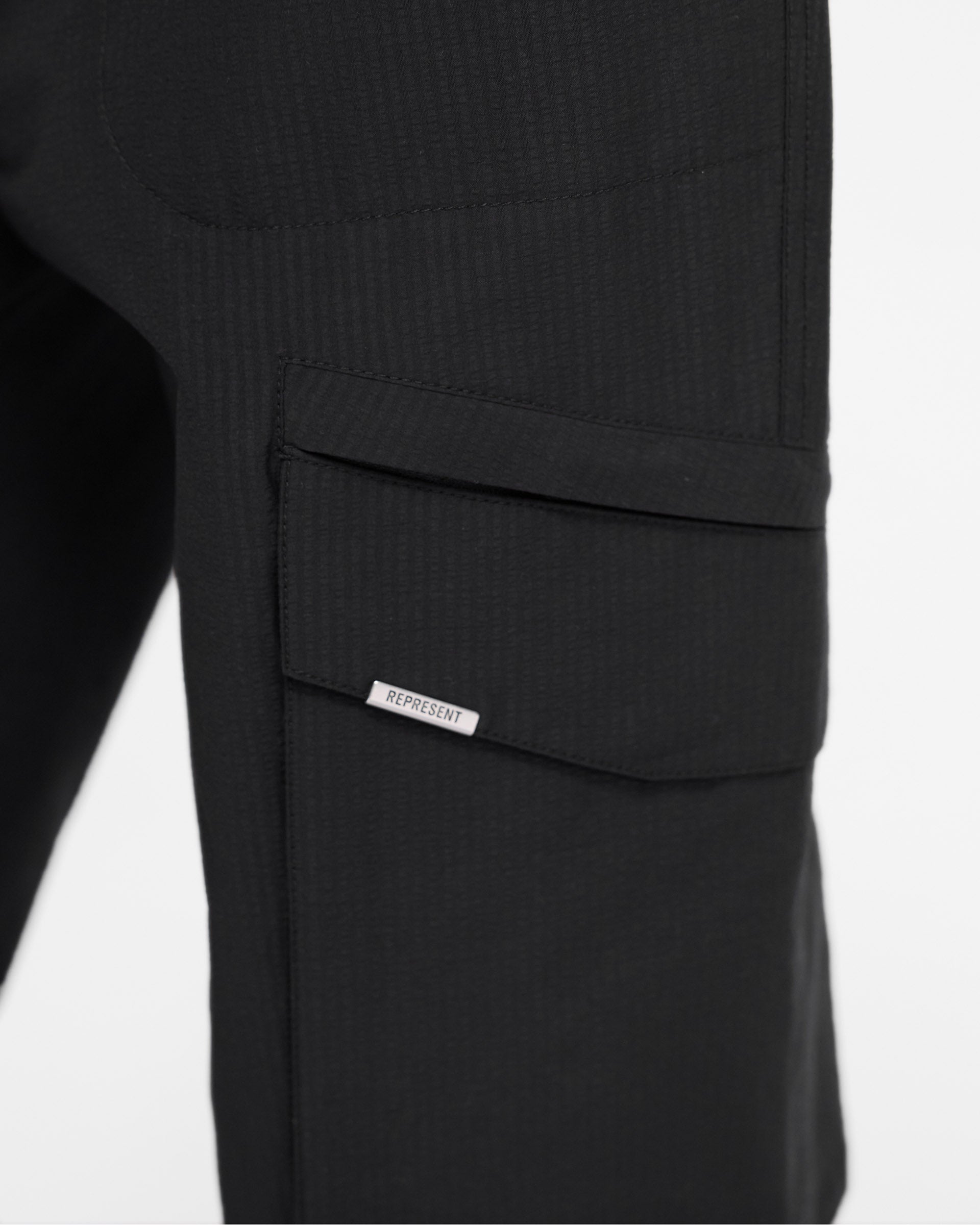 Man wearing black cargo pants on a plain white background | Tech Cargo Pant in Jet Black | Cargo pants with elasticated waistband and diagonal pockets | FW24 Pants | Represent Clo