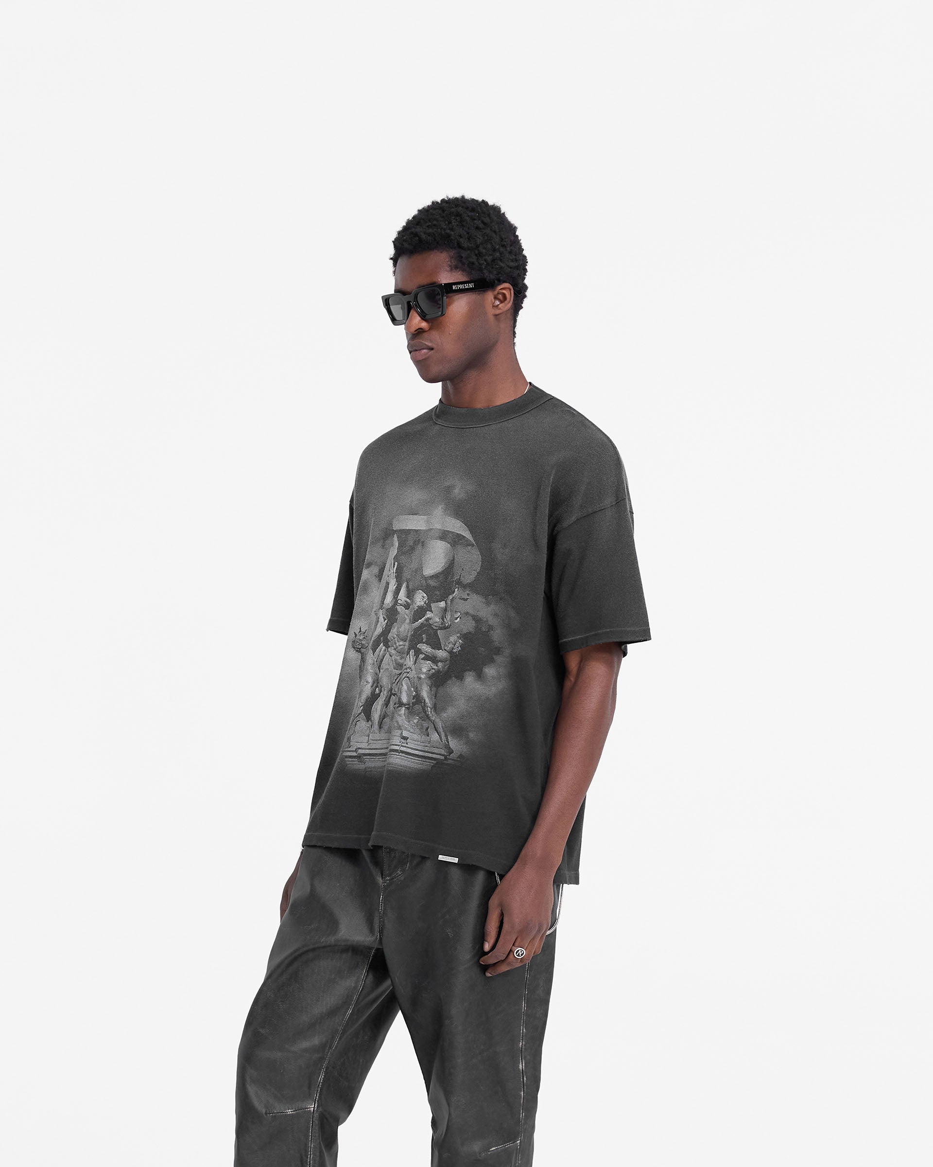 Man wearing a black t-shirt on a plain white background | Atlas T-Shirt in Stained Black | Luxury oversized t-shirt with puff and screen print graphics | FW24 T-Shirts | Represent Clo