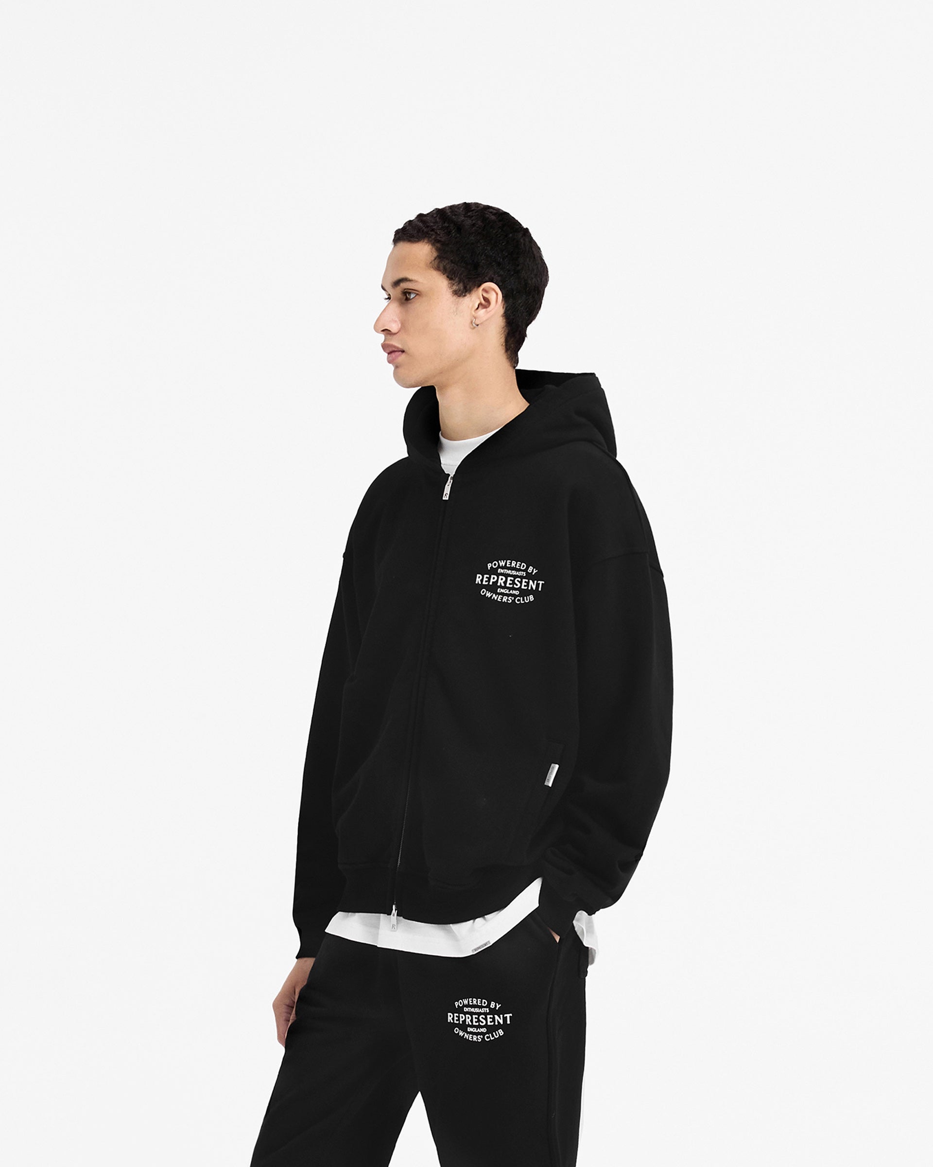 Man wearing a black zip-up hoodie on a plain white background | Represent Owners Club Stamp Zip Up Hoodie in Jet Black | Oversized fit hoodie with high build branding and double ended zip | Owners Club Hoodies | Represent Clo