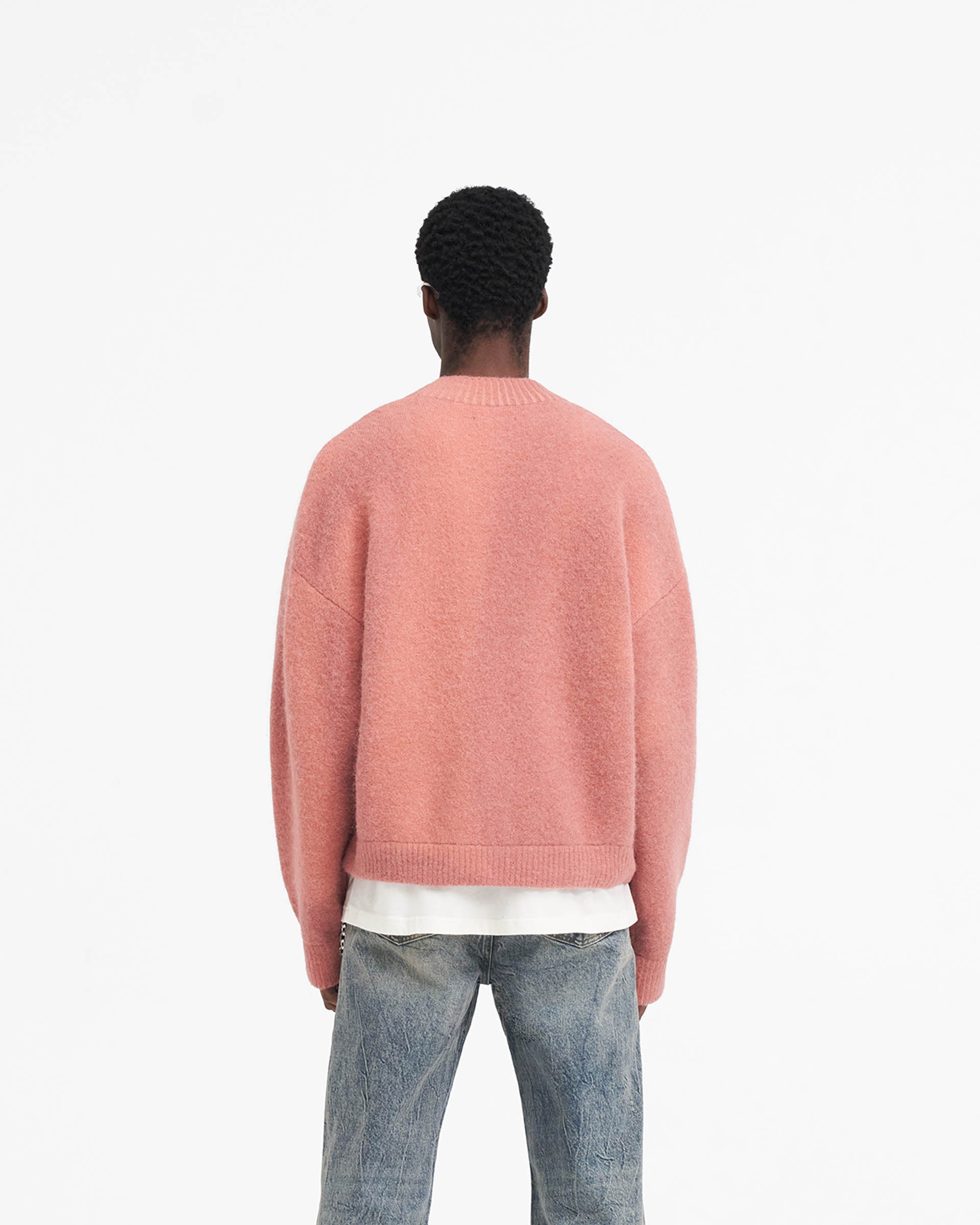 Man wearing a pink sweater on a plain white background | Sprayed Horizons Sweater in Sunrise | Alpaca and wool blend oversized sweater with ribbed detailing | SS24 Knitwear | Represent Clo
