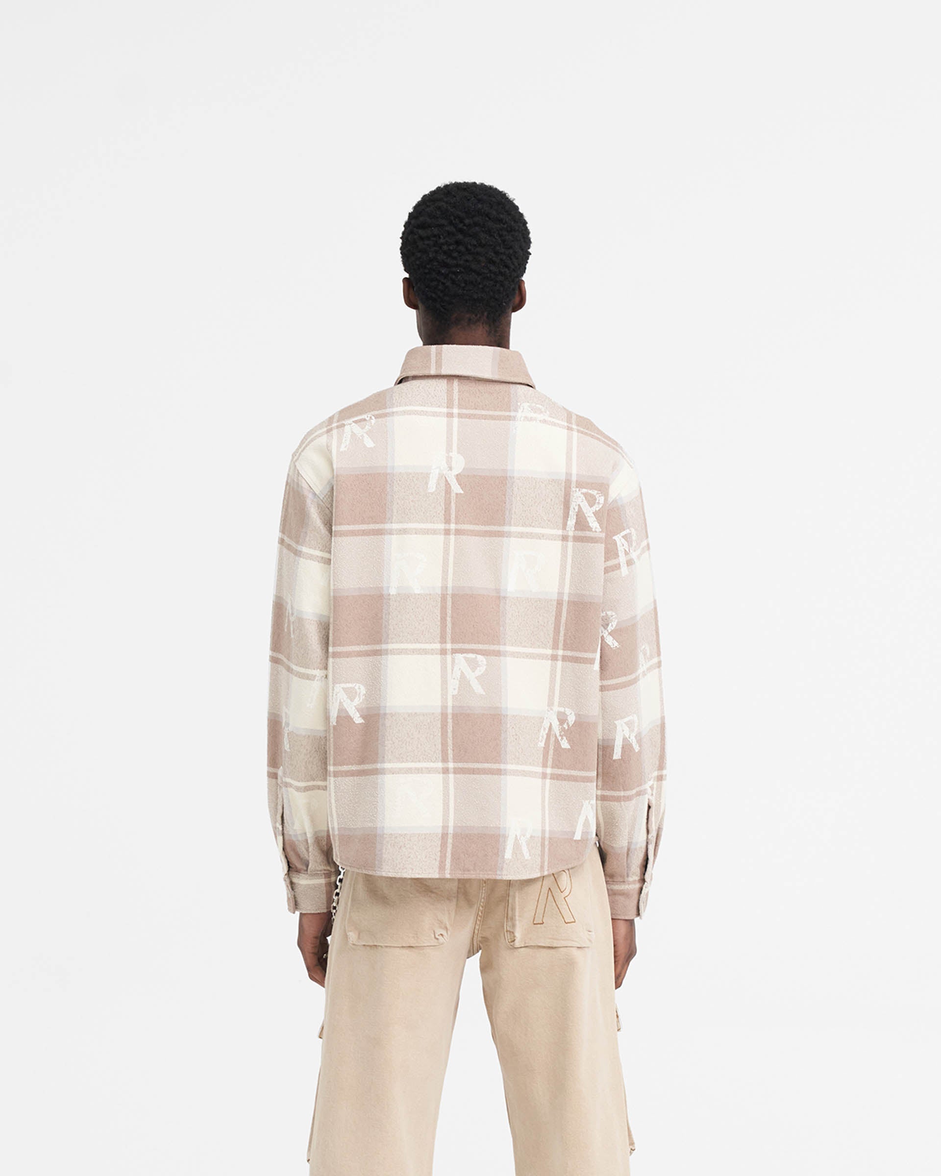 Man wearing a brown check shirt on a plain white background | All Over Initial Flannel Shirt in Cashmere | Oversized cotton blend shirt with distressed logos and Cobrax popper fastenings | SS24 Shirts | Represent Clo