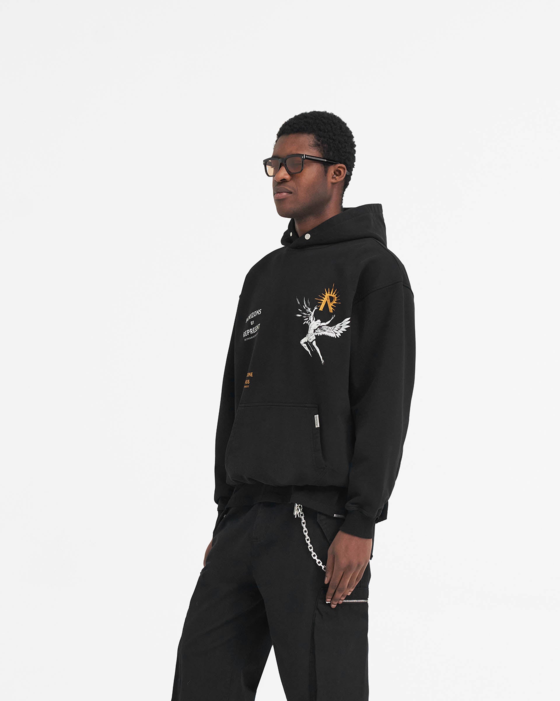 Man wearing an oversized black hoodie with Icarus graphic on a plain white background | Icarus Hoodie in Jet Black | Luxury hoodie with ribbed hem and cuffs | SS24 Hoodies | Represent Clo