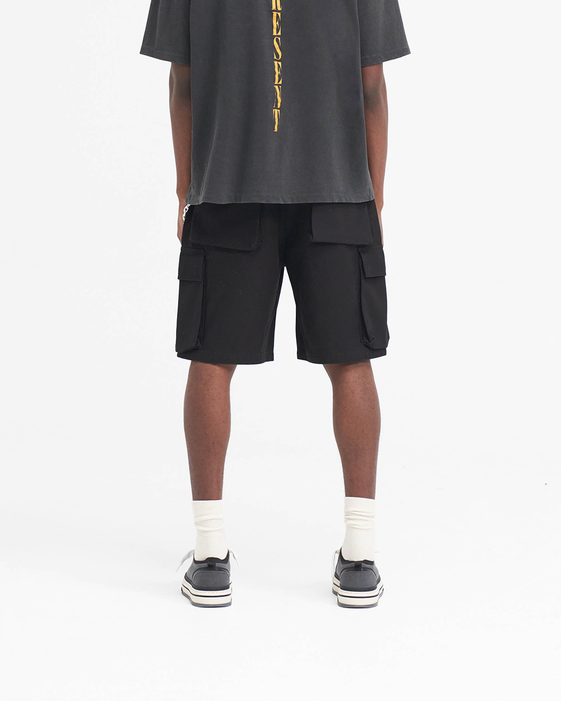 Man wearing black baggy cargo shorts on a plain white background | Baggy Cotton Cargo Short in Black | Baggy fit shorts with 3D oversized pockets | SS24 Shorts | Represent Clo