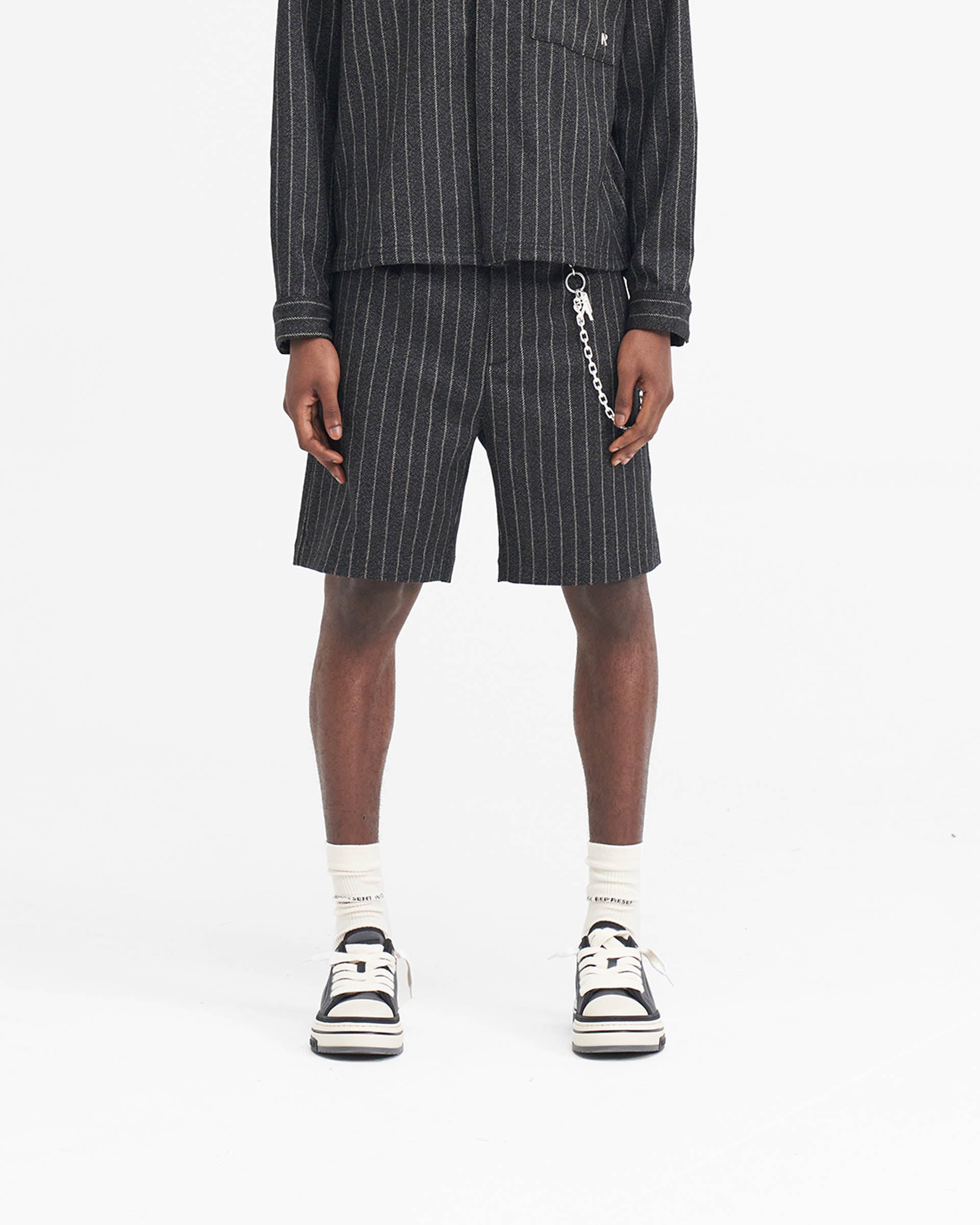 Man wearing black pinstripe shorts on a plain white background | Tailored Short in Black Pinstripe | Tailored shorts with wide leg fit | SS24 Shorts | Represent Clo