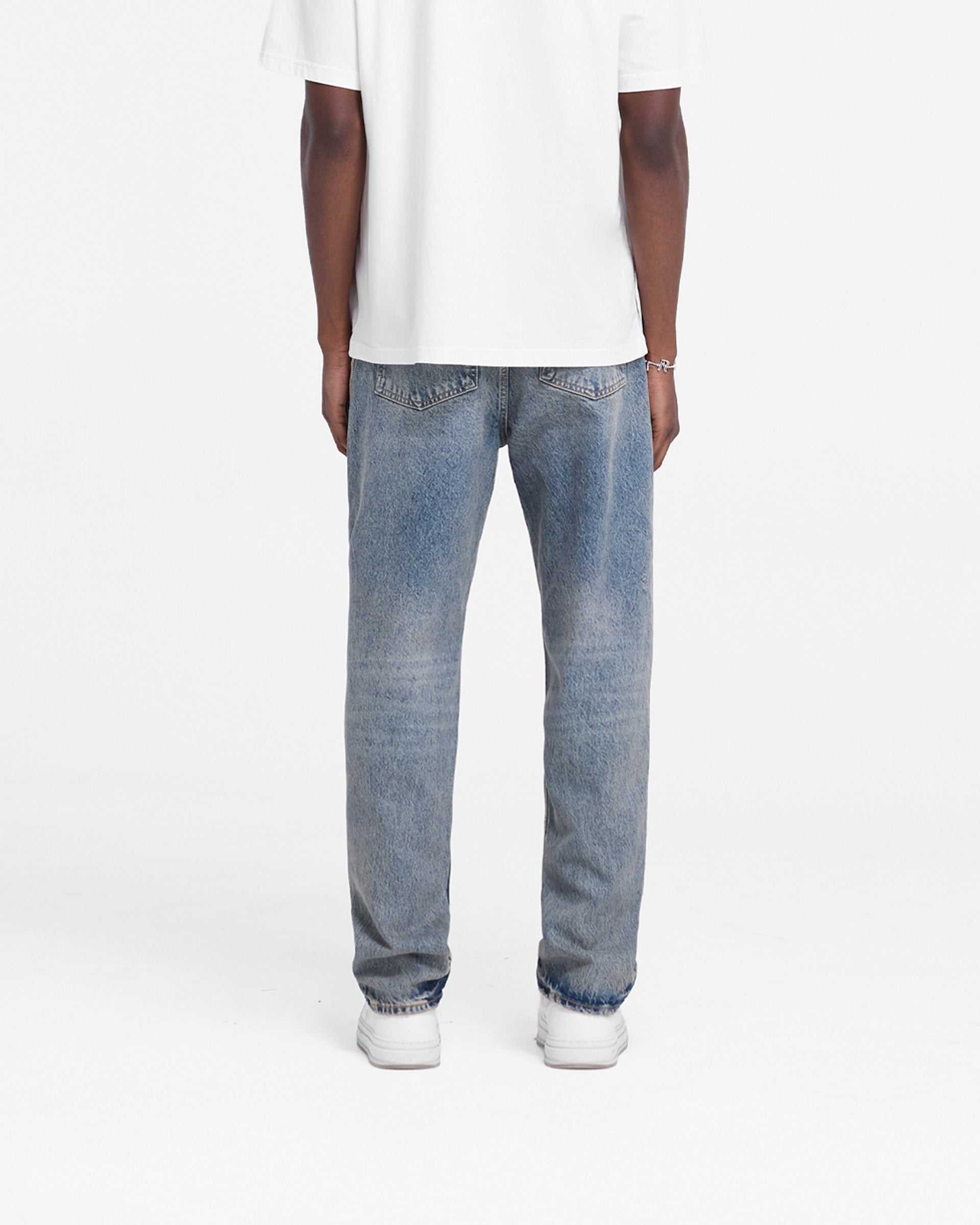 Man wearing mid blue jeans on a plain white background | R2 Straight Leg Denim in Mid Blue | Straight leg jeans with embroidered initial | FW24 Denim | Represent Clo