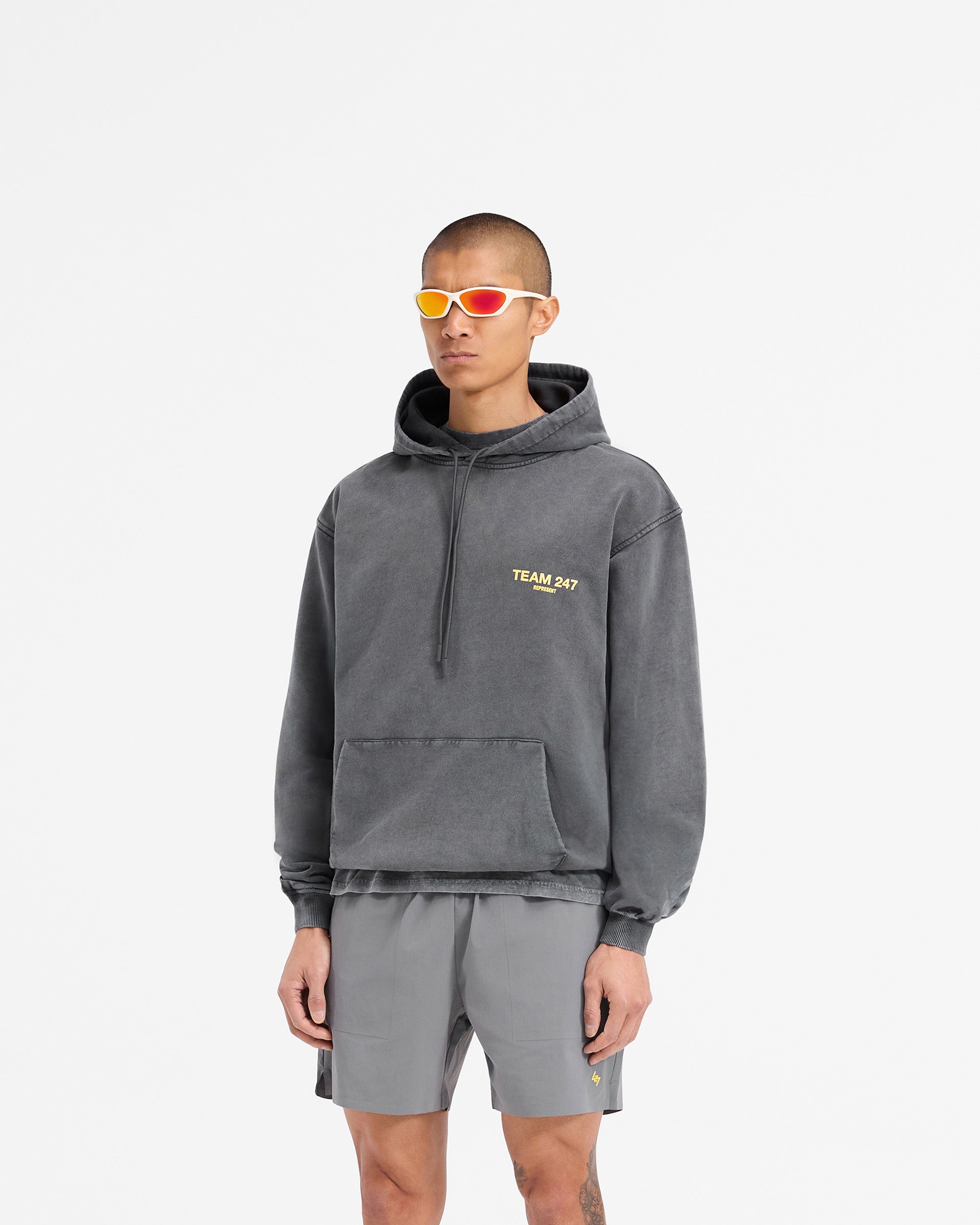Man wearing an oversized grey hoodie with yellow accents on a plain white background | Team 247 Oversized Hoodie in Pewter Lemon | Oversized hoodie with ribbed cuffs and Team 247 branding | 247 Hoodies | Represent Clo