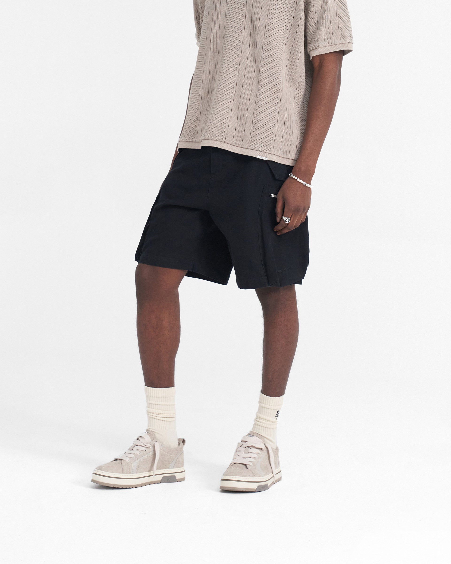 Man wearing baggy black shorts on a plain white background | Workshop Short in Black | Shorts with 3D back and cargo pockets | SS24 Shorts | Represent Clo